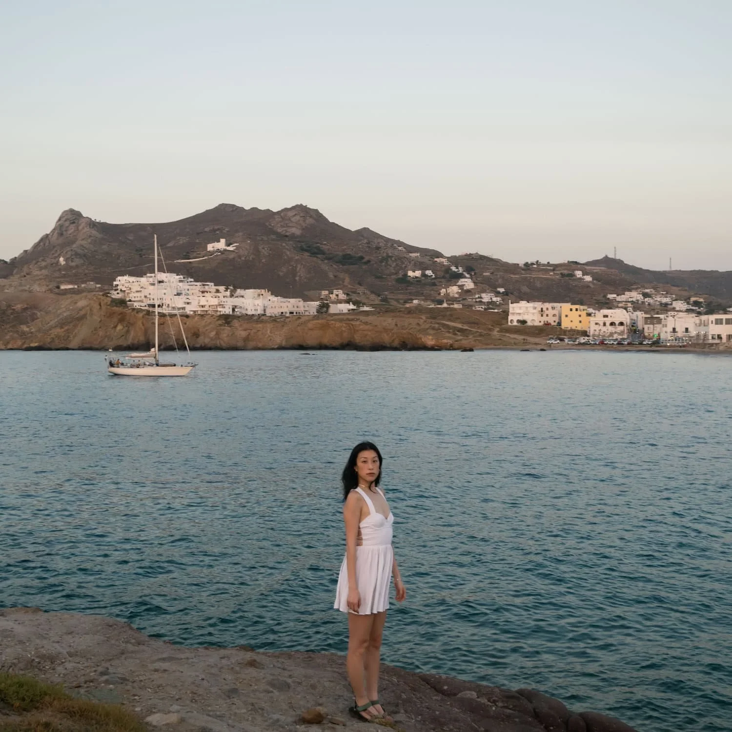 Woman standing by the waterfront on a Greek island at sunset. The best eSIM for Greece offers reliable coverage during your trip.