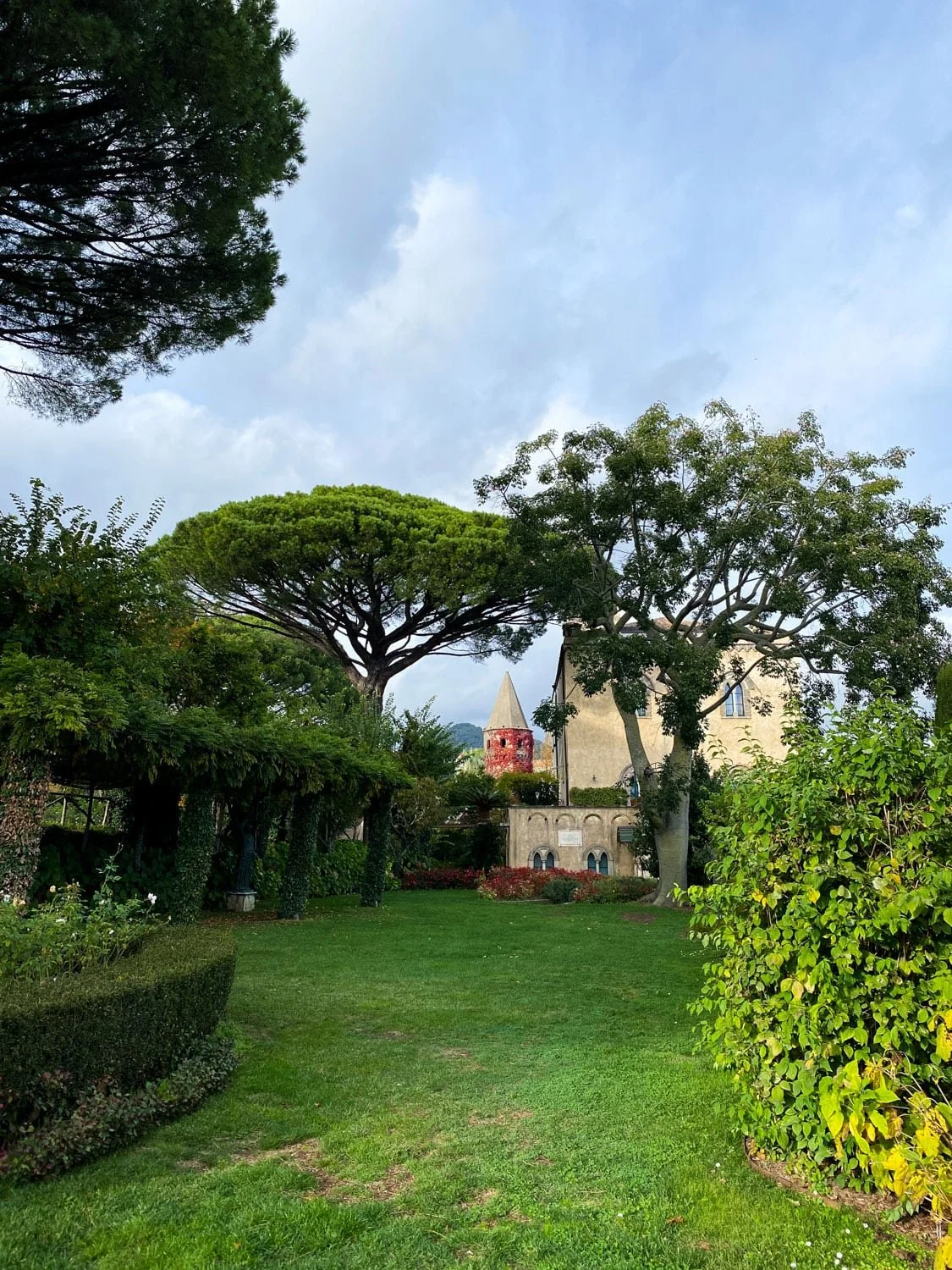 Lush green garden with tall umbrella pine trees and a historic villa in the background in Ravello. Manicured lawns and Mediterranean landscaping create a peaceful atmosphere for visitors exploring things to do in Ravello.