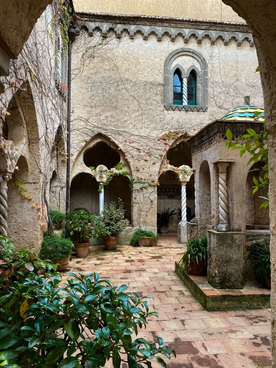 Quiet stone courtyard with climbing vines, potted plants, and arched walkways inside a historic Ravello villa. The peaceful garden setting reflects the timeless charm of things to do in Ravello.