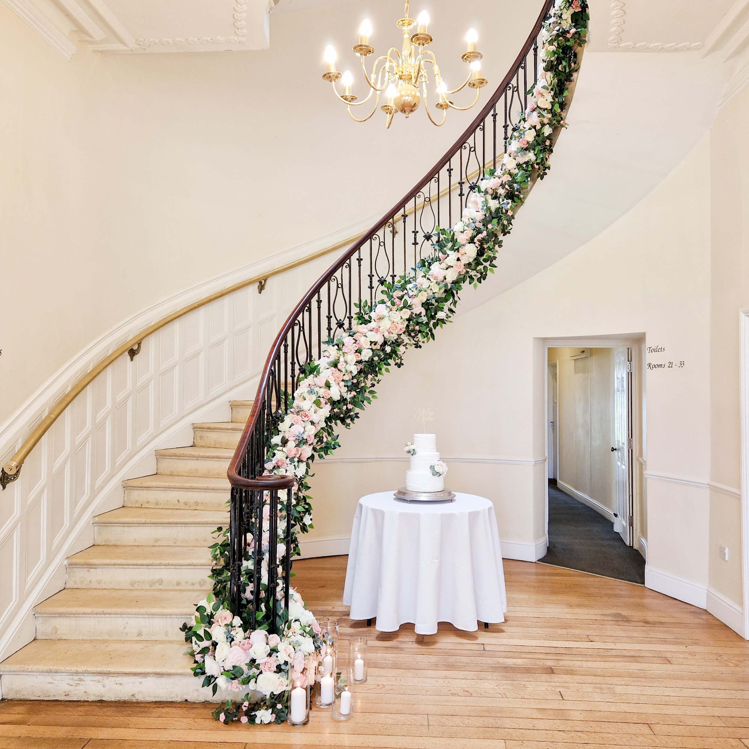 the gran staircase at Eastinngton Park, Gloucestershire, styled with a blush pink garland, showcasing the cake table