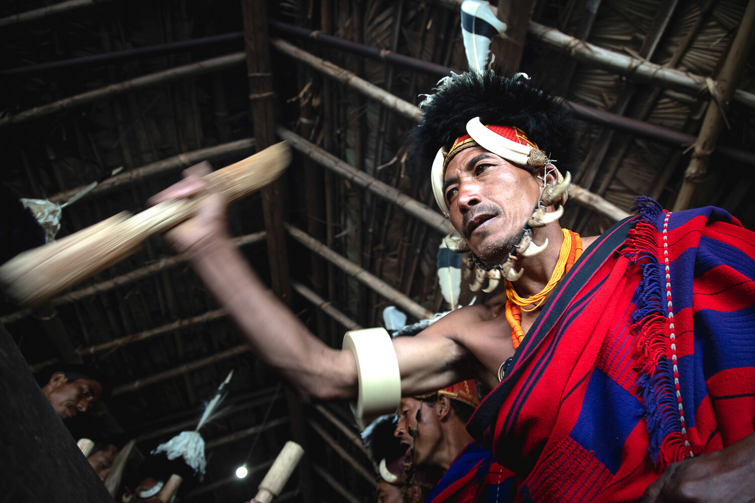 naga worrior playing traditional wooden log drum inside morung during hornbill festival in nagaland