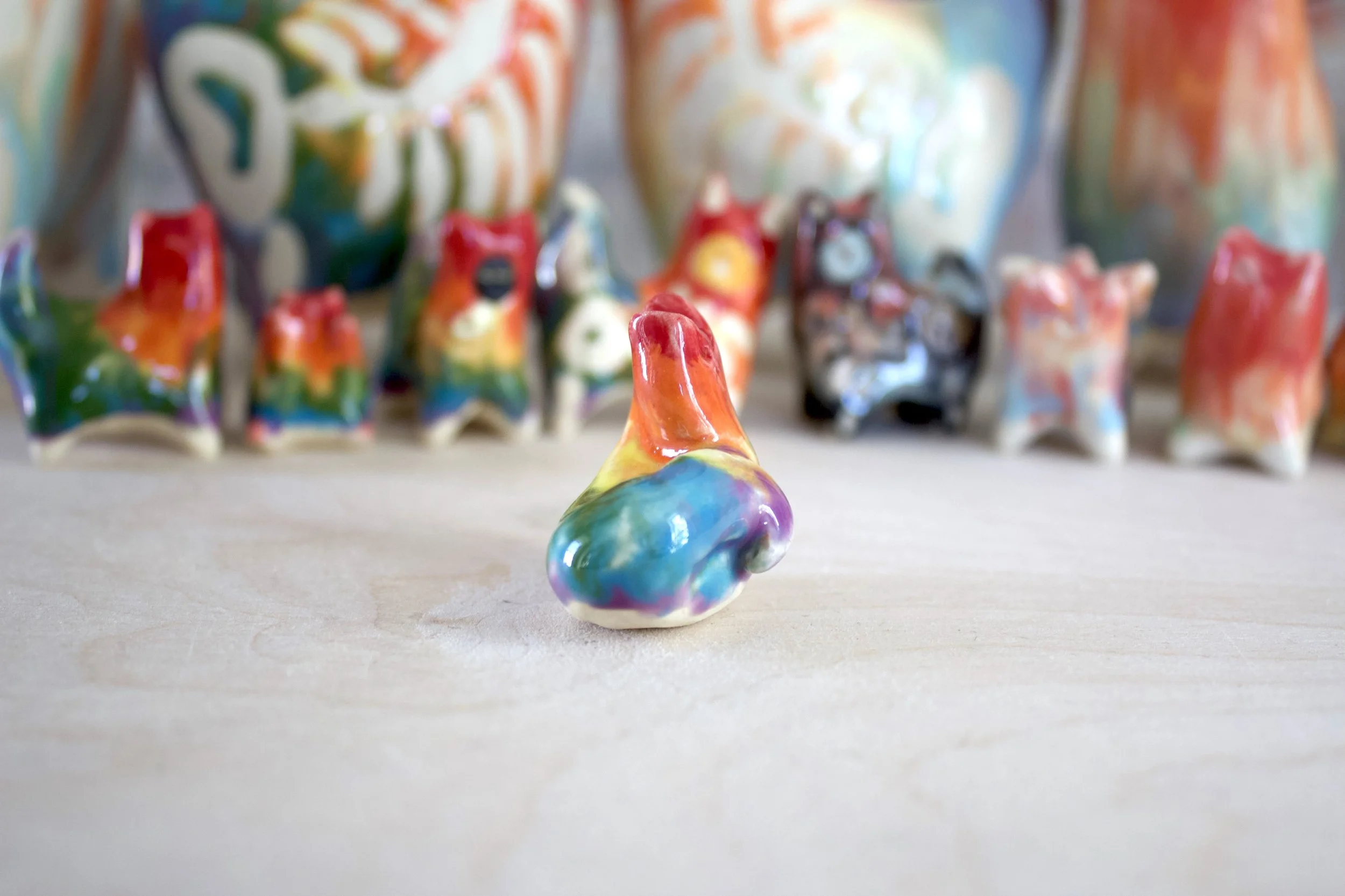 Three-quarter view of a handmade ceramic rainbow snake cat sculpture with colorful sculpted details.