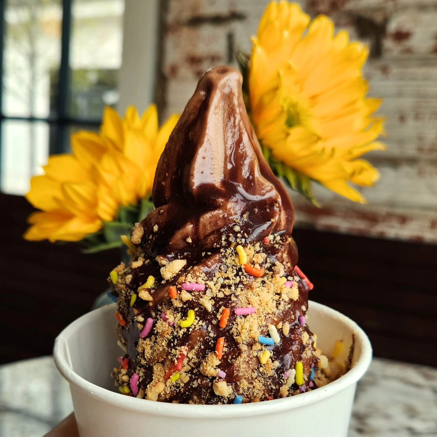 It may be cloudy outside, but it's nice and cozy in our caf&eacute; seating! Here's our oatmilk chocolate decked out in fudge sauce and peanut crunch 🌻🍦🍫🥜