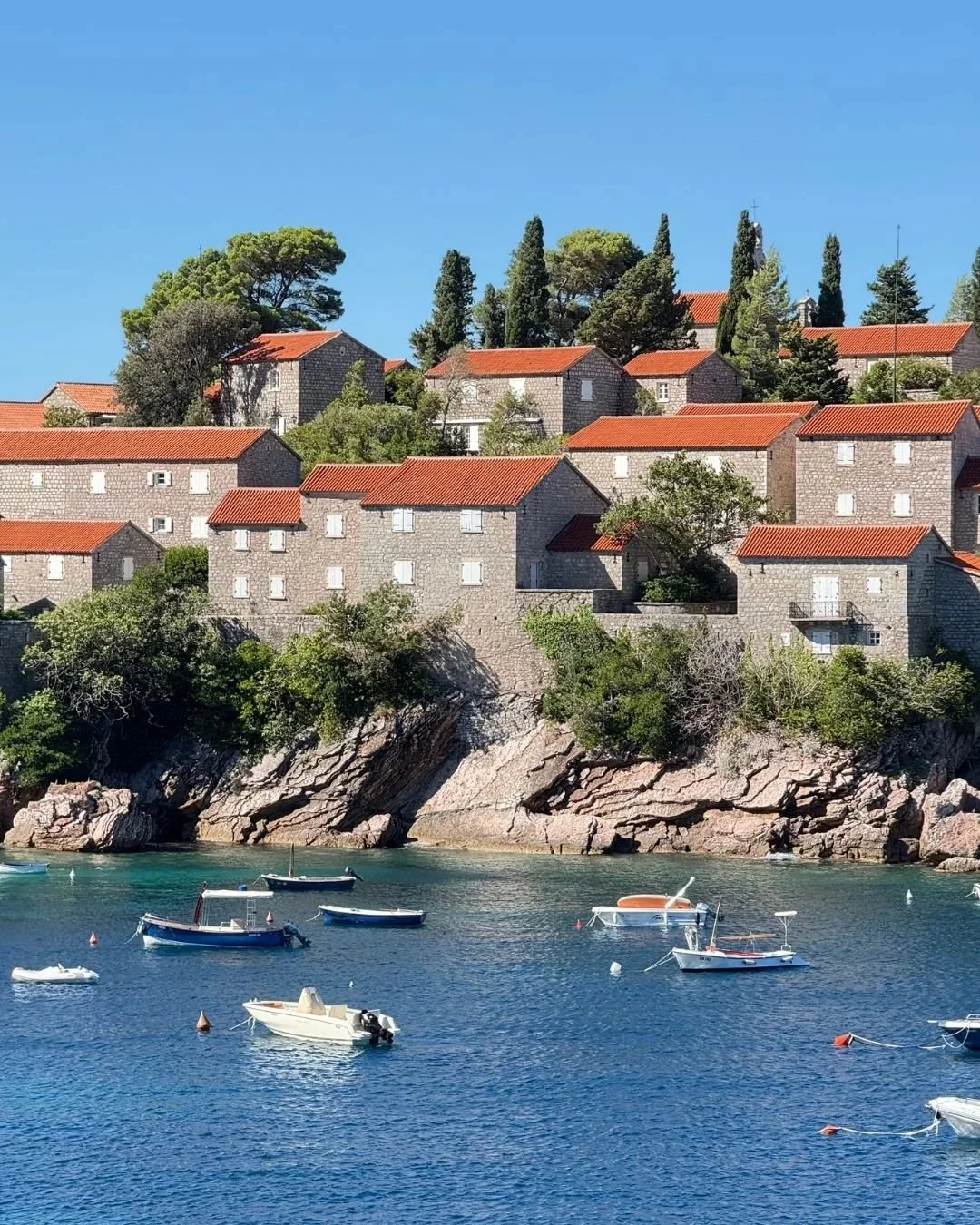 Sveti Stefan island in Montenegro with boats on clear blue Adriatic water