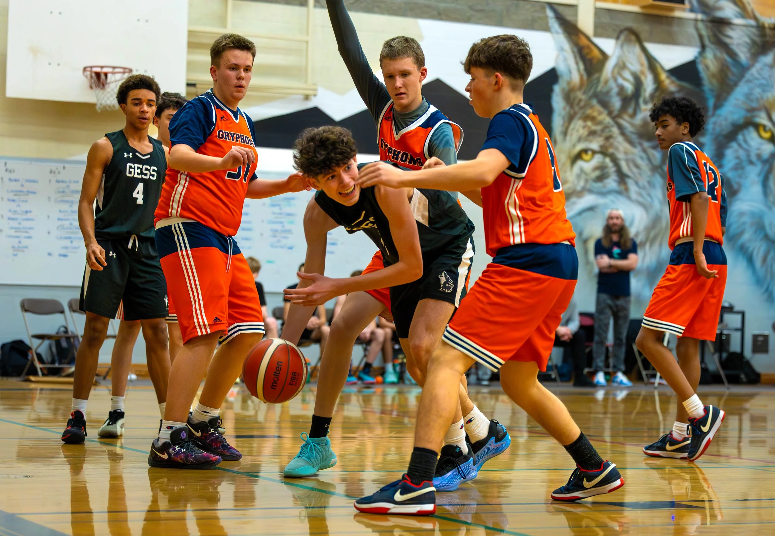 Young boys playing basketball on an indoor court with colorful lion mural in the background