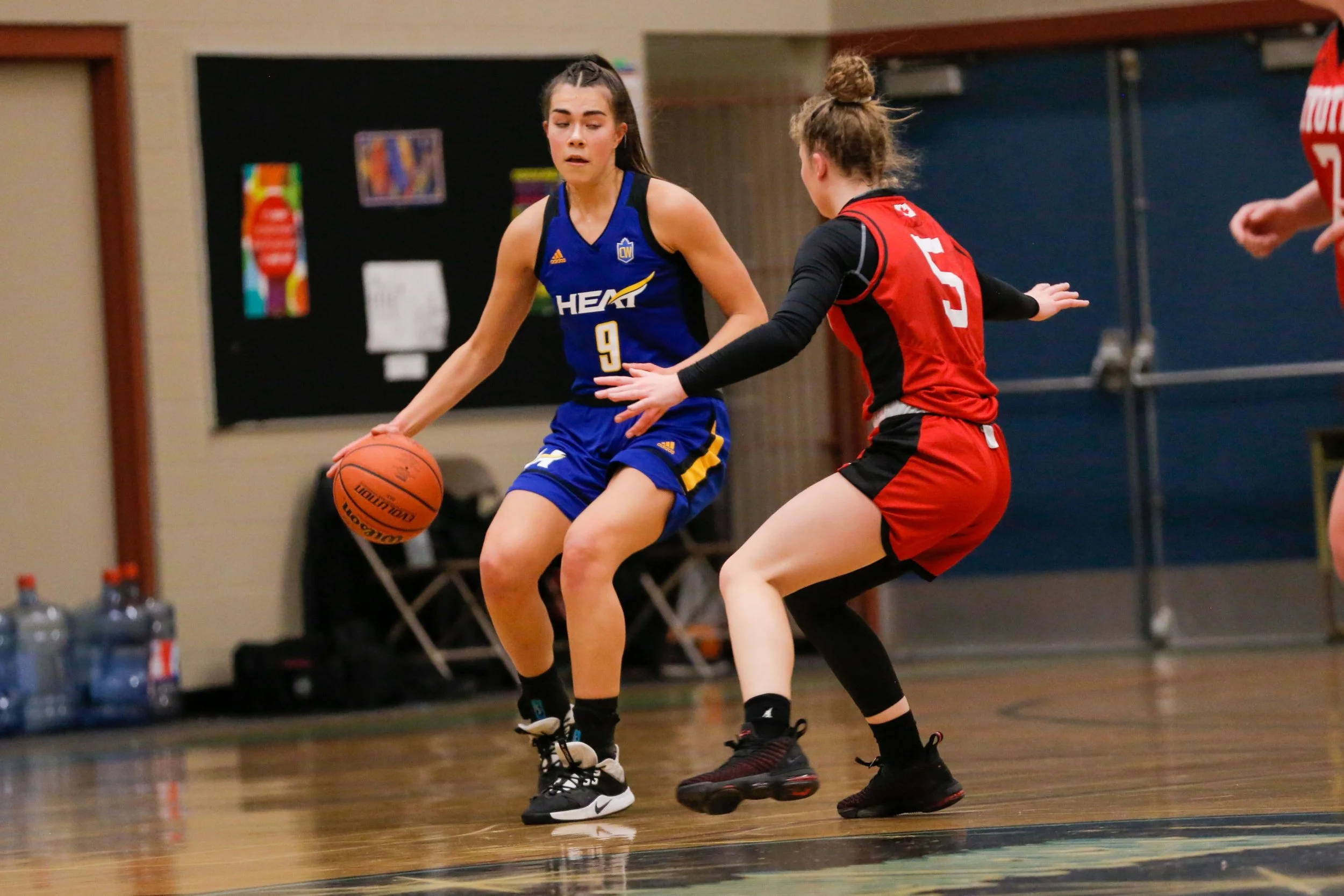 Two female basketball players competing for the ball during a game inside a gymnasium.