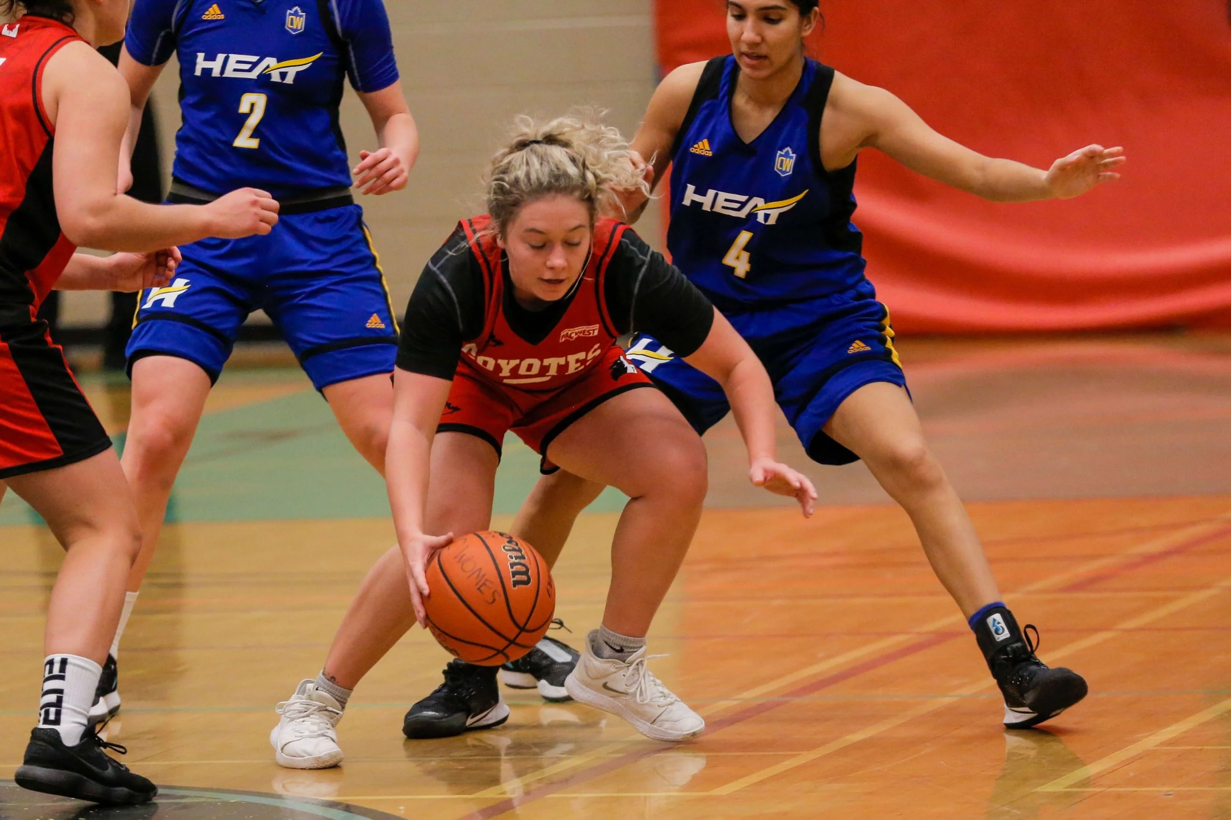 Women playing basketball, with one player crouching to grab the basketball while others try to defend.