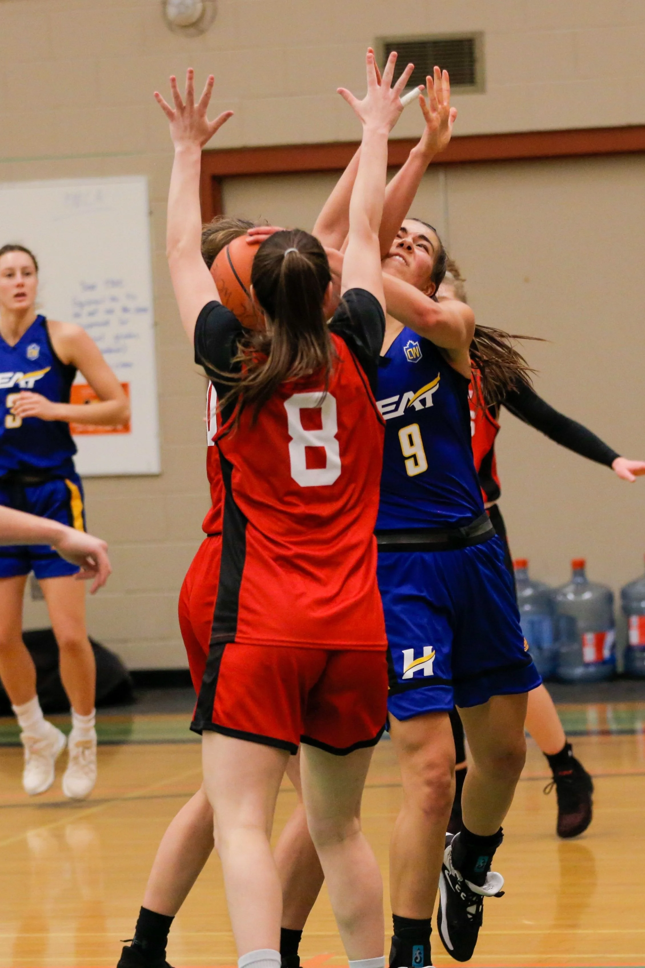 Girls playing basketball during a game, with one girl attempting a shot while others try to block or defend.