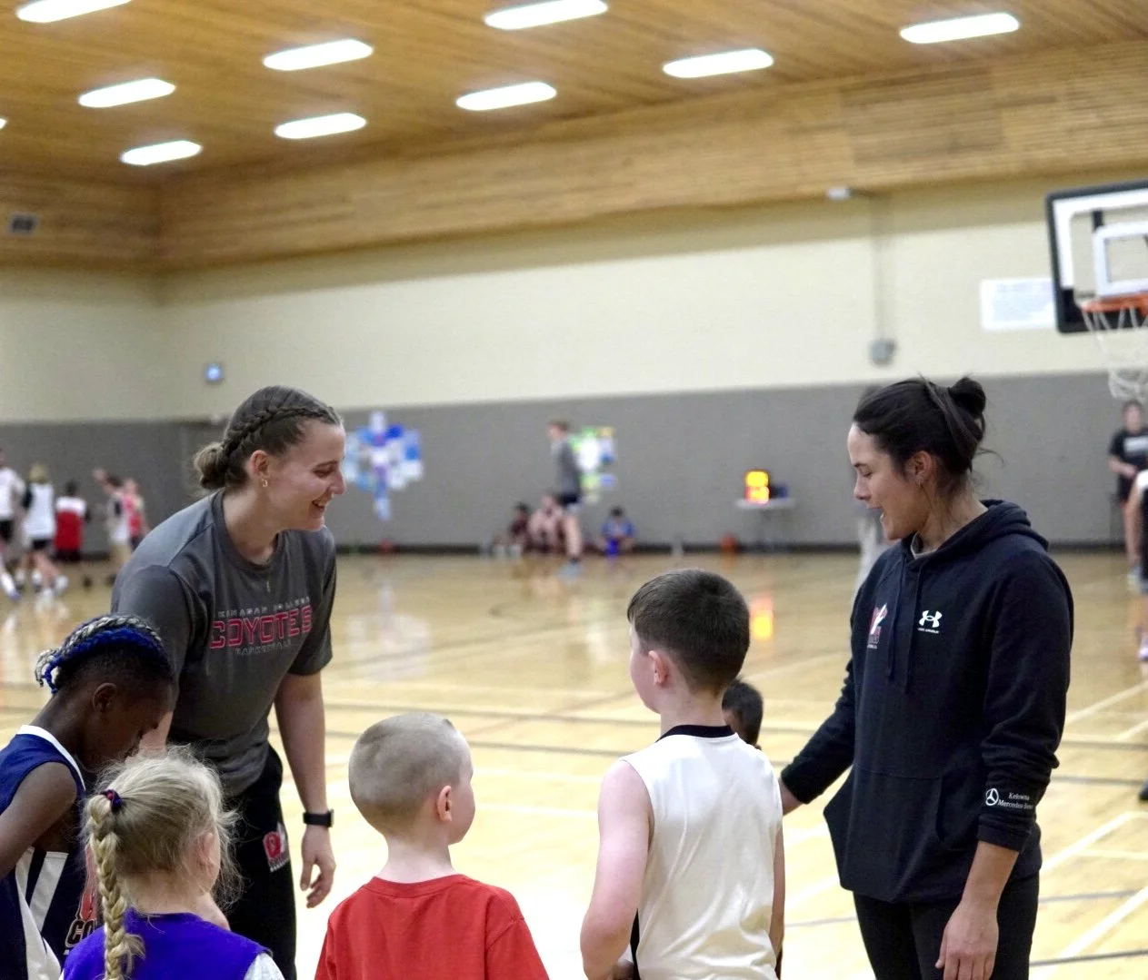 Women coaches talking to young boys and girls during a basketball practice in a gymnasium.