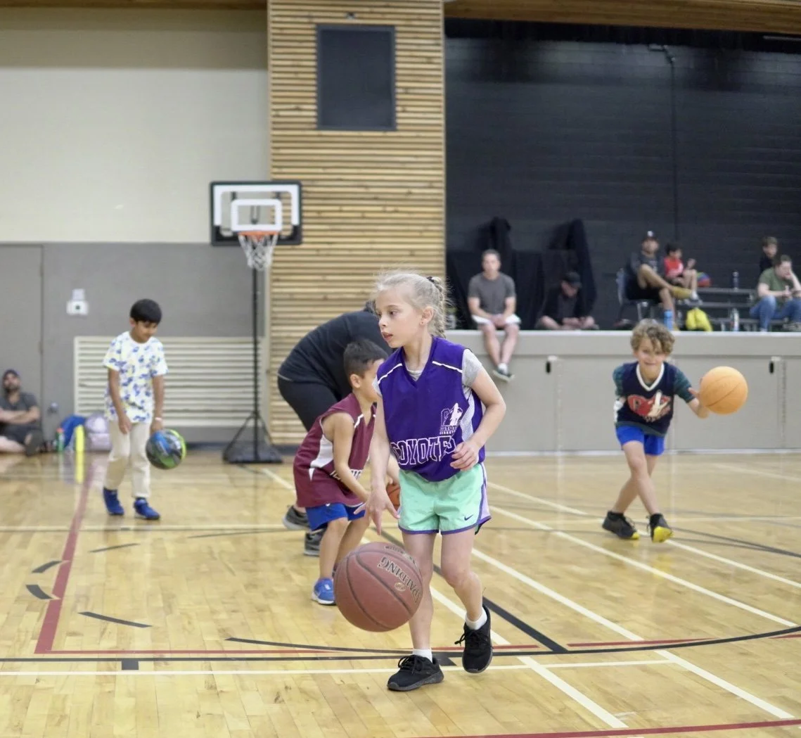 Group of children playing and practicing basketball in an indoor gymnasium.