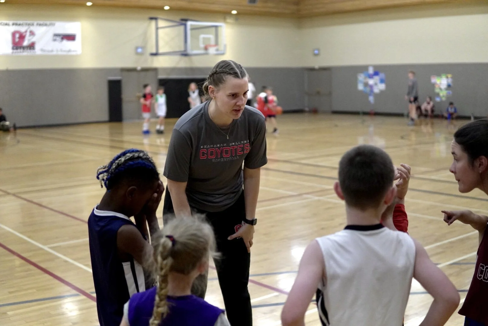 A female basketball coach instructs young players during a practice session in an indoor gymnasium.