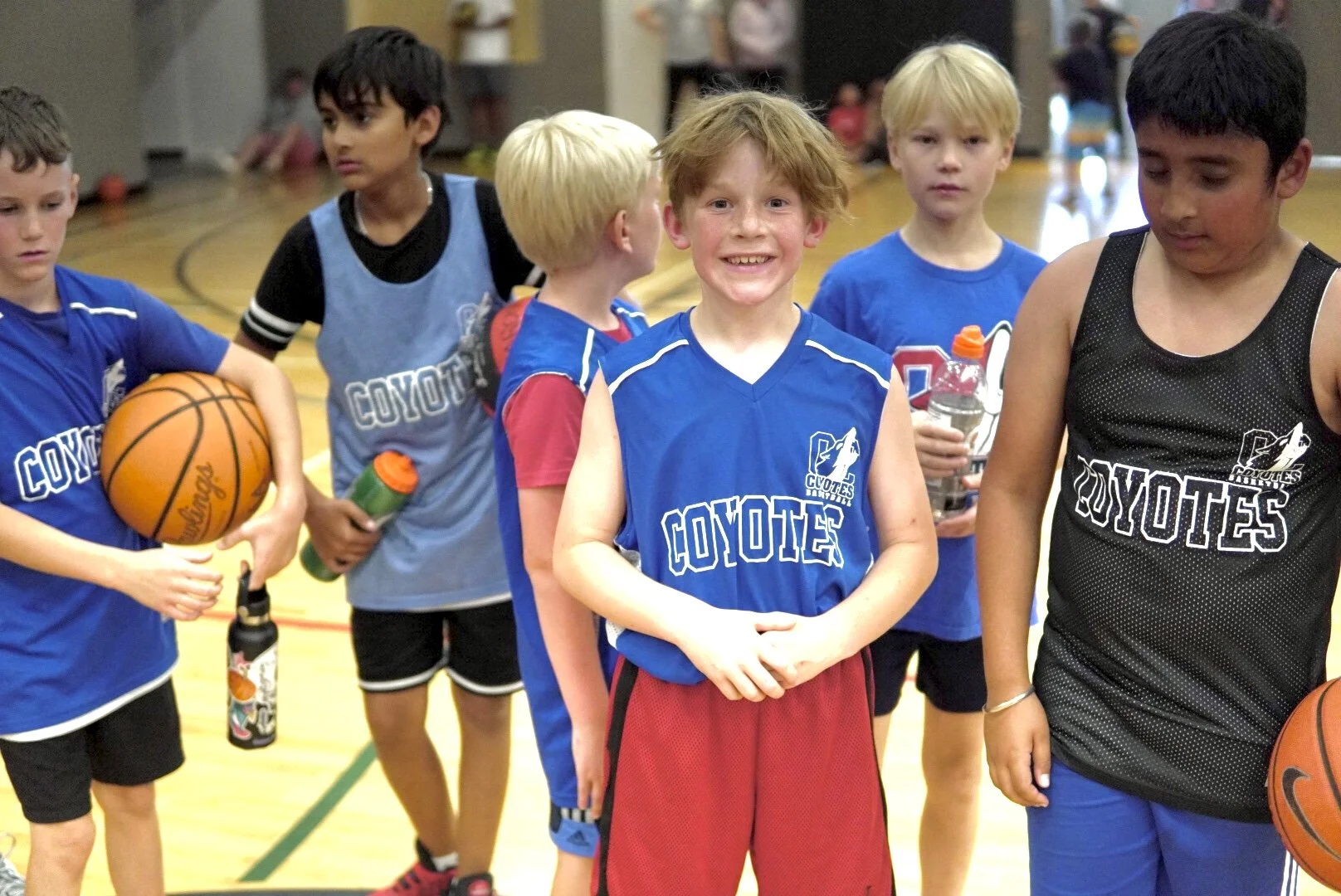 Group of young boys wearing basketball jerseys with 'Coyotes' logo, standing on a gymnasium court, holding basketballs and water bottles.