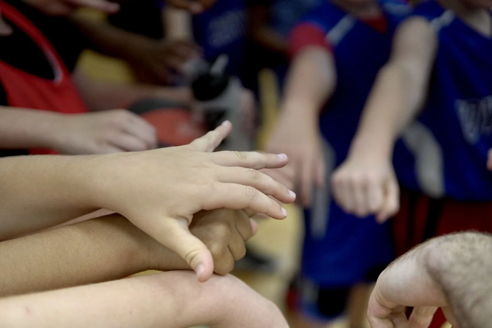 A group of children with their hands extended forward, making contact or pointing towards something, in a collective gesture.
