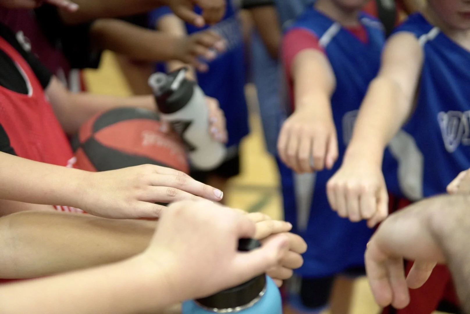 Children wearing sports uniforms holding basketballs and extending their fists in a huddle.