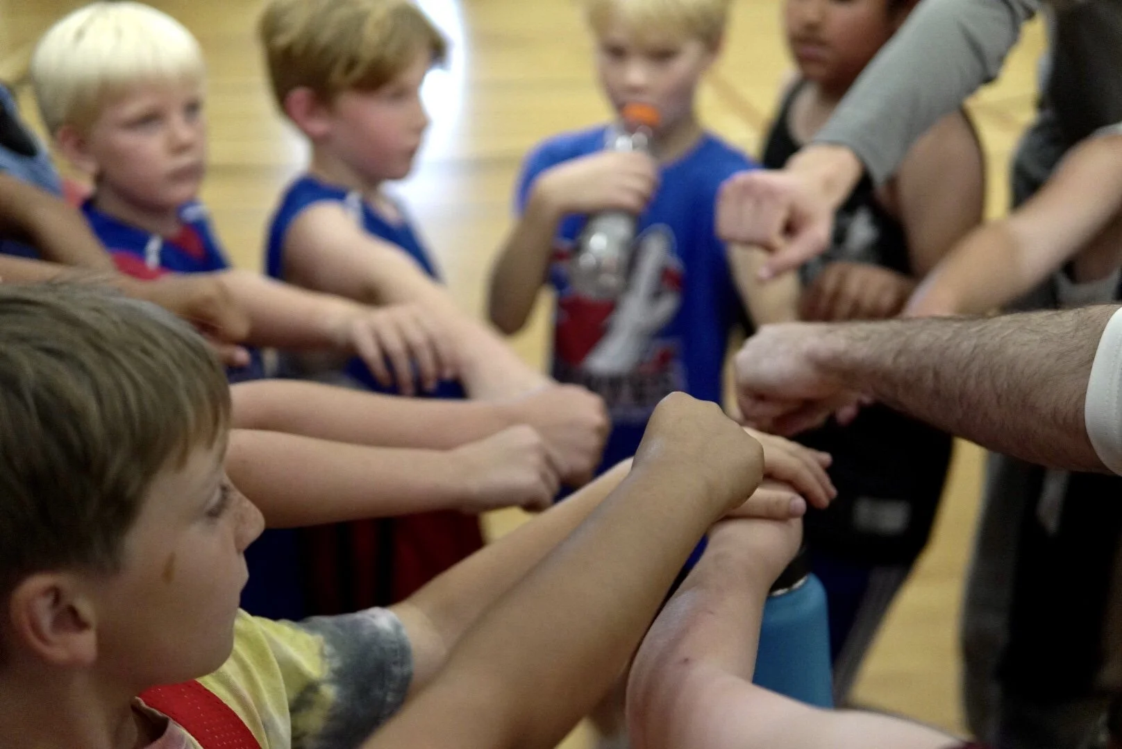 Group of children with outstretched arms in a gymnasium, participating in a team activity with an adult.