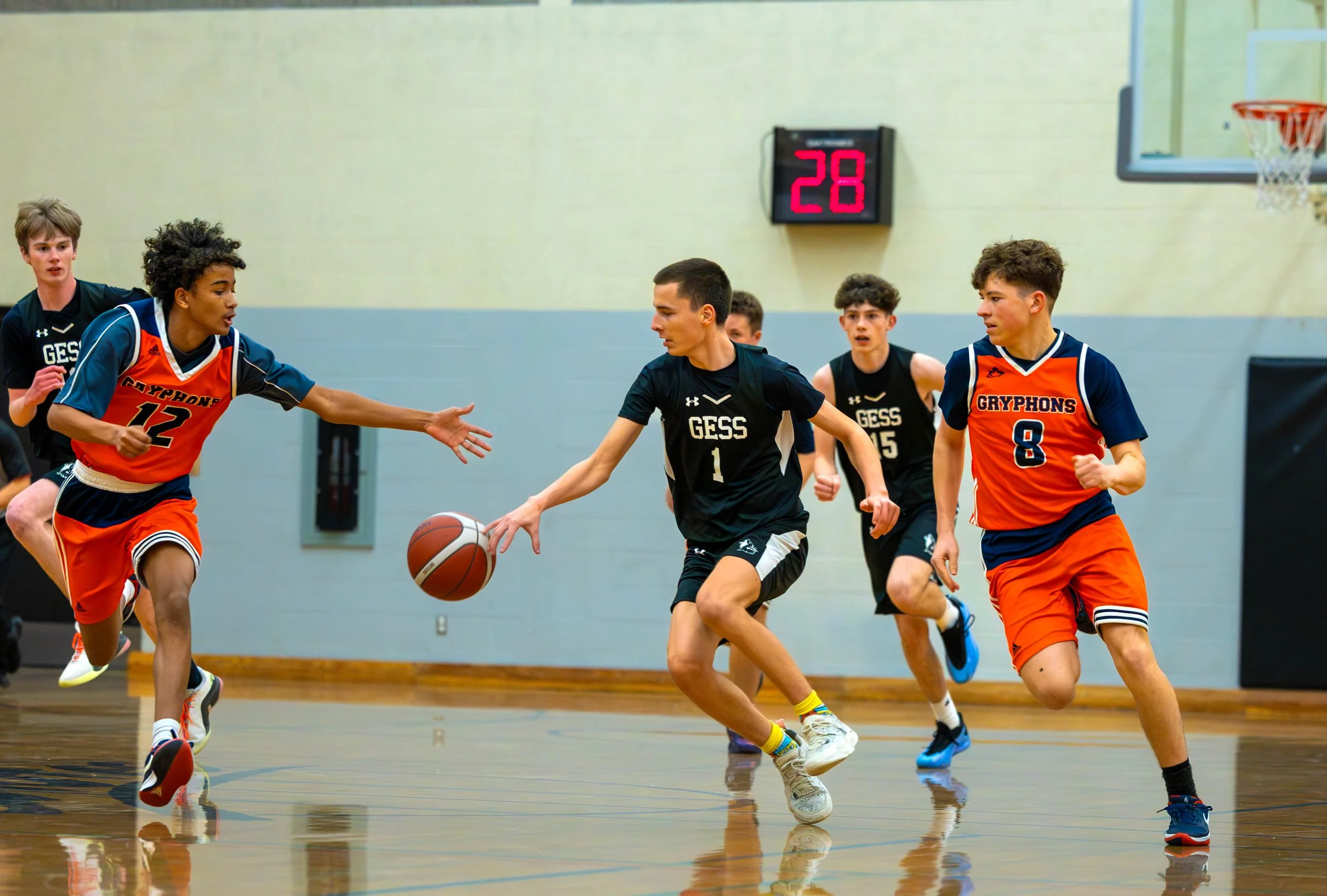 Young boys playing basketball in a gym, with one player passing the ball while others are running on the court.