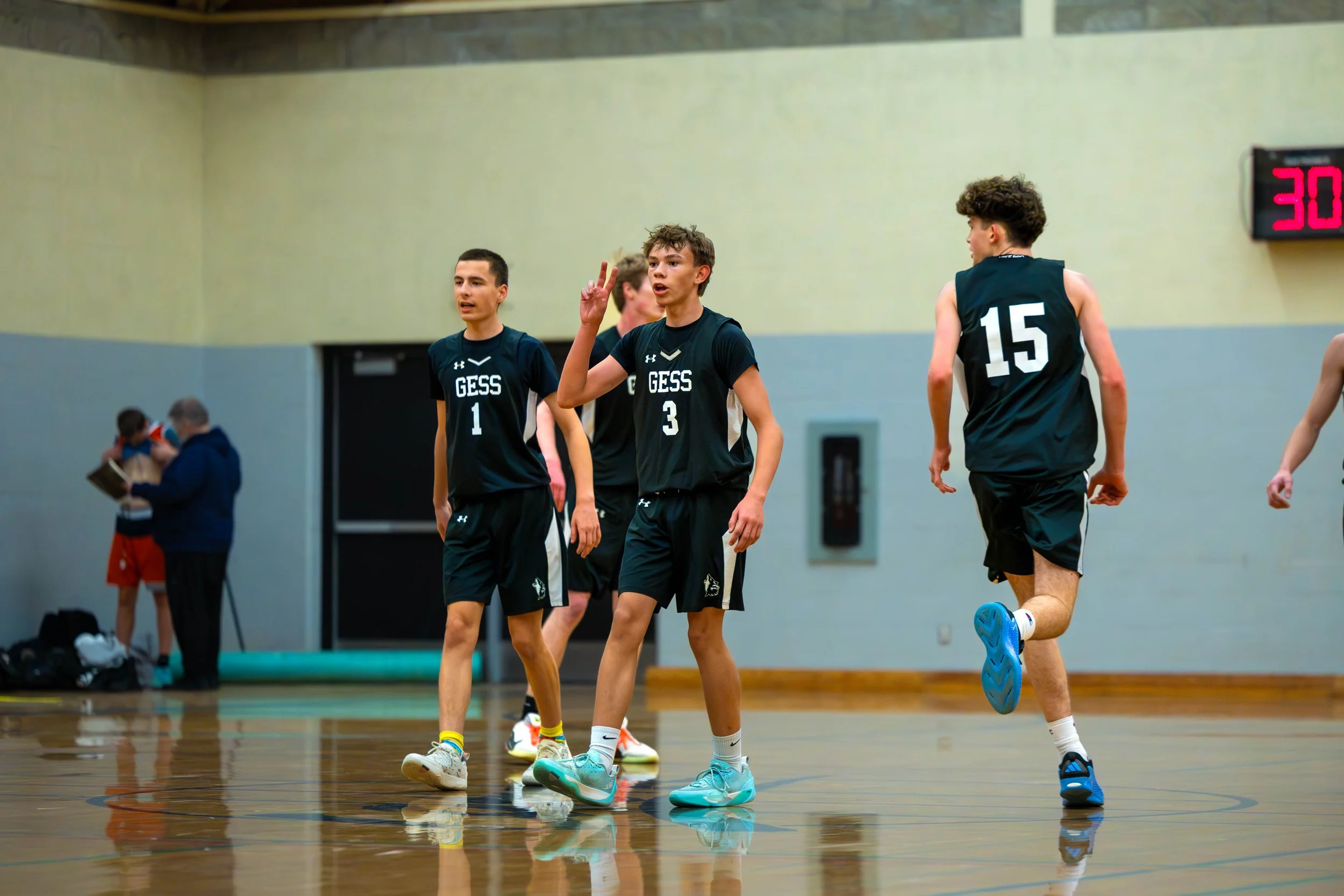 Young boys playing basketball on an indoor court, wearing black jerseys with 'GESS' and numbers, and standing near the middle of the court.