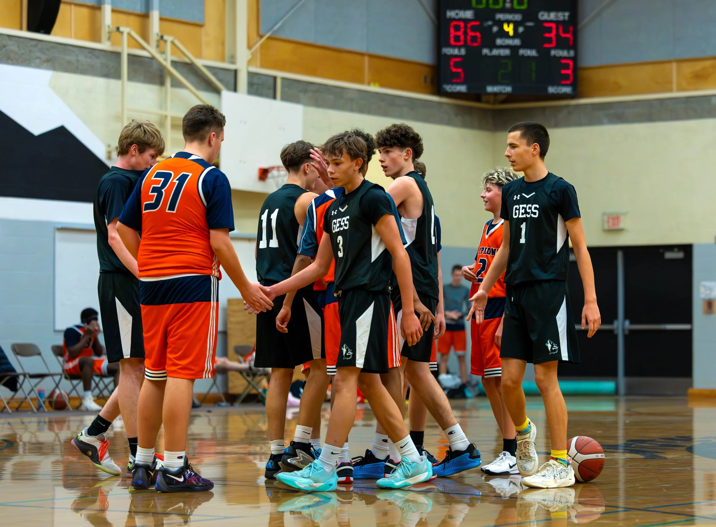 Young basketball players huddle together on a basketball court during a game, with the scoreboard showing 86-34 in the background.
