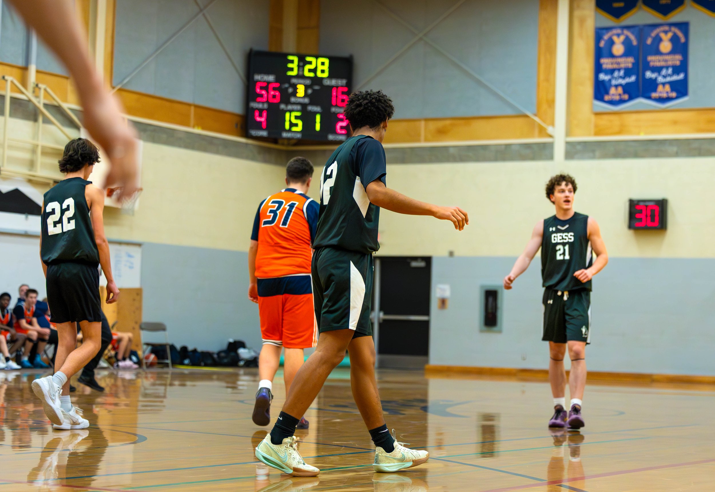 Kids playing basketball in an indoor gymnasium with scoreboard showing 3:28 on the clock, score 56-16, and players on the court.