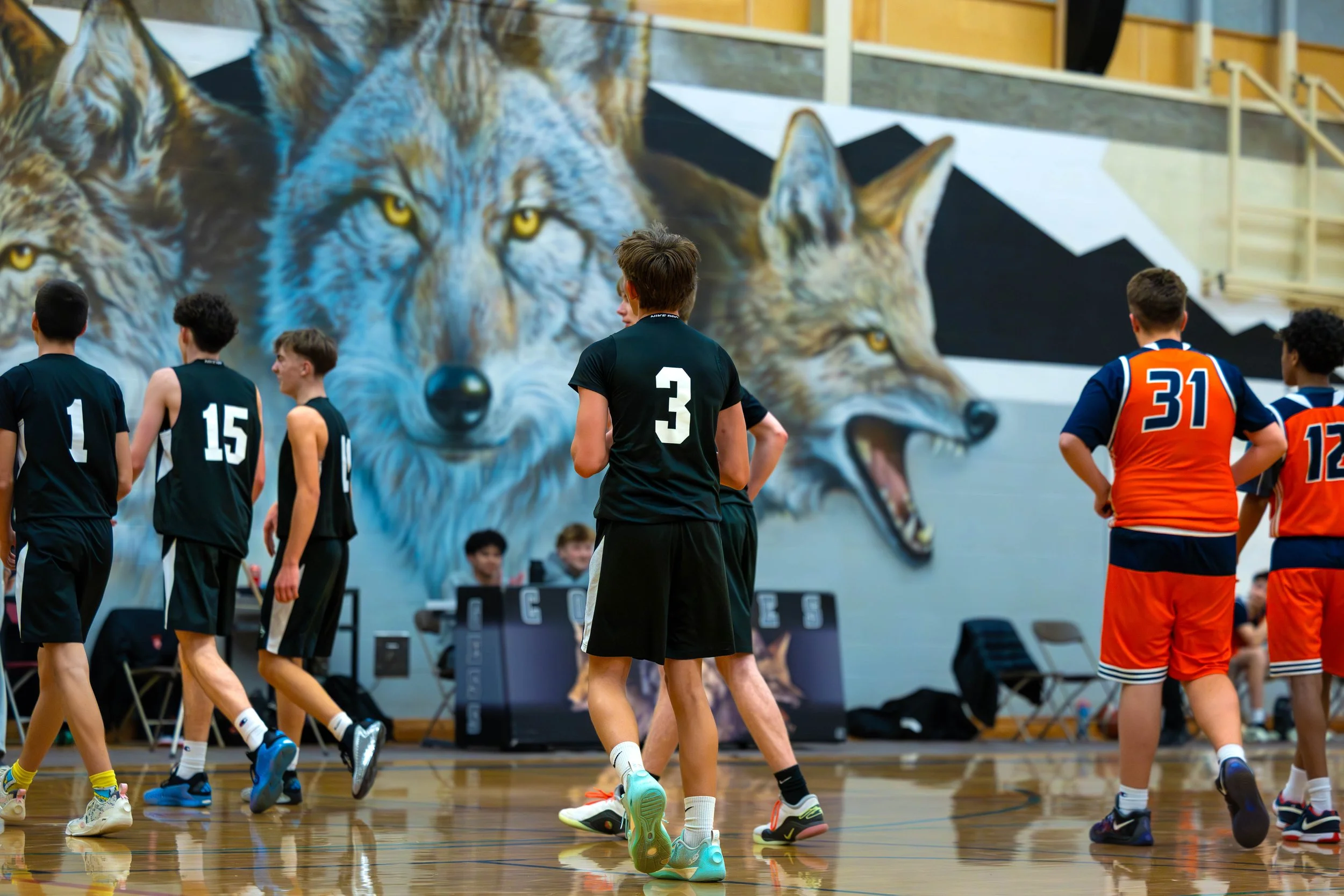 Young basketball players on an indoor court with a large mural of a wolf in the background.