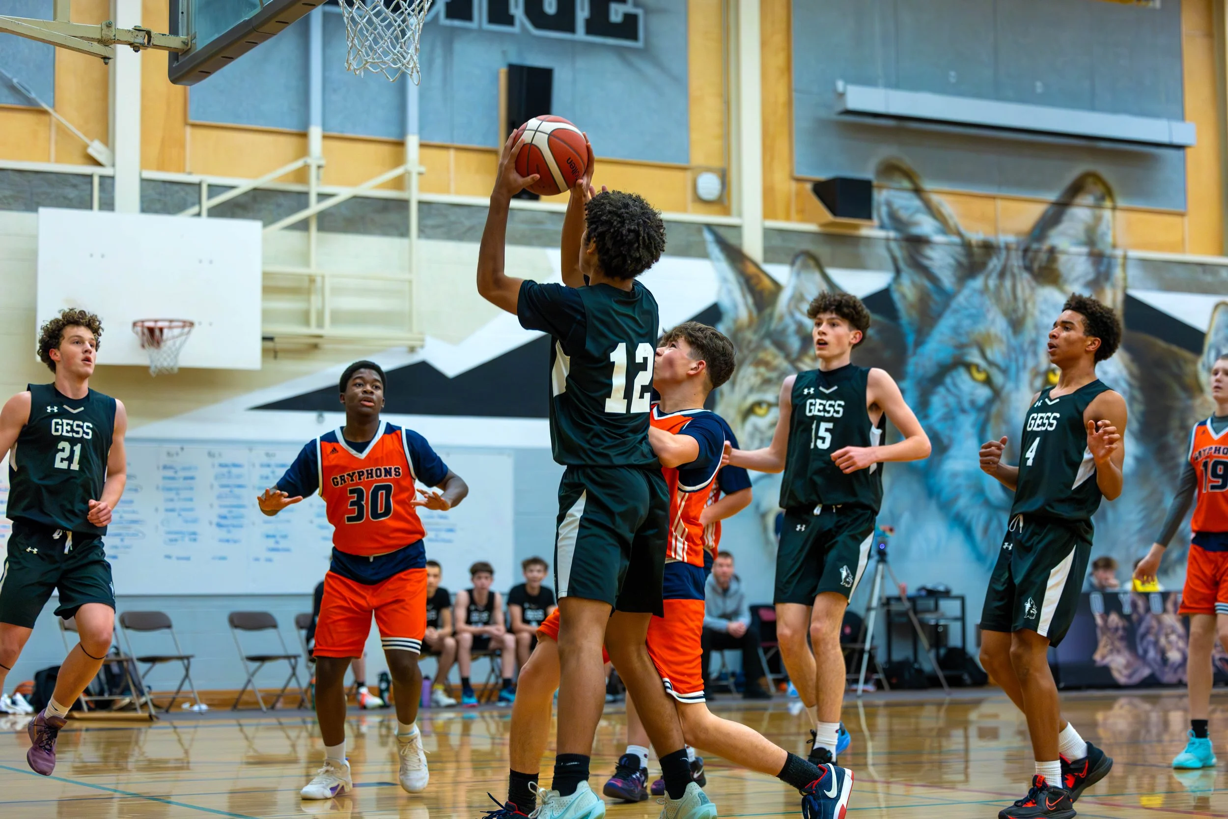 Kids playing basketball in an indoor gym, with one player about to take a shot and others defending.