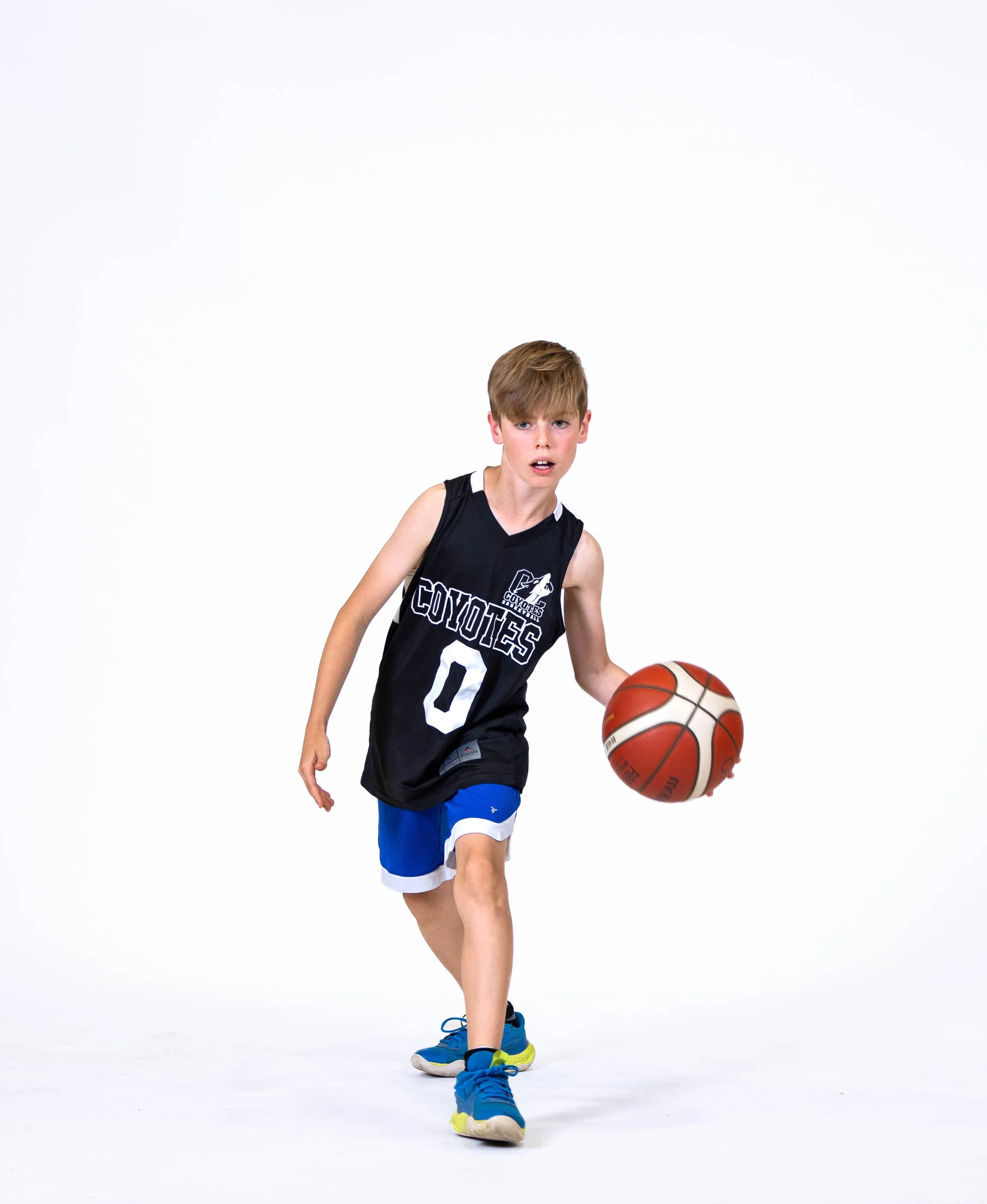 A young boy in a black basketball uniform dribbling an orange basketball with white and black lines on a white background.