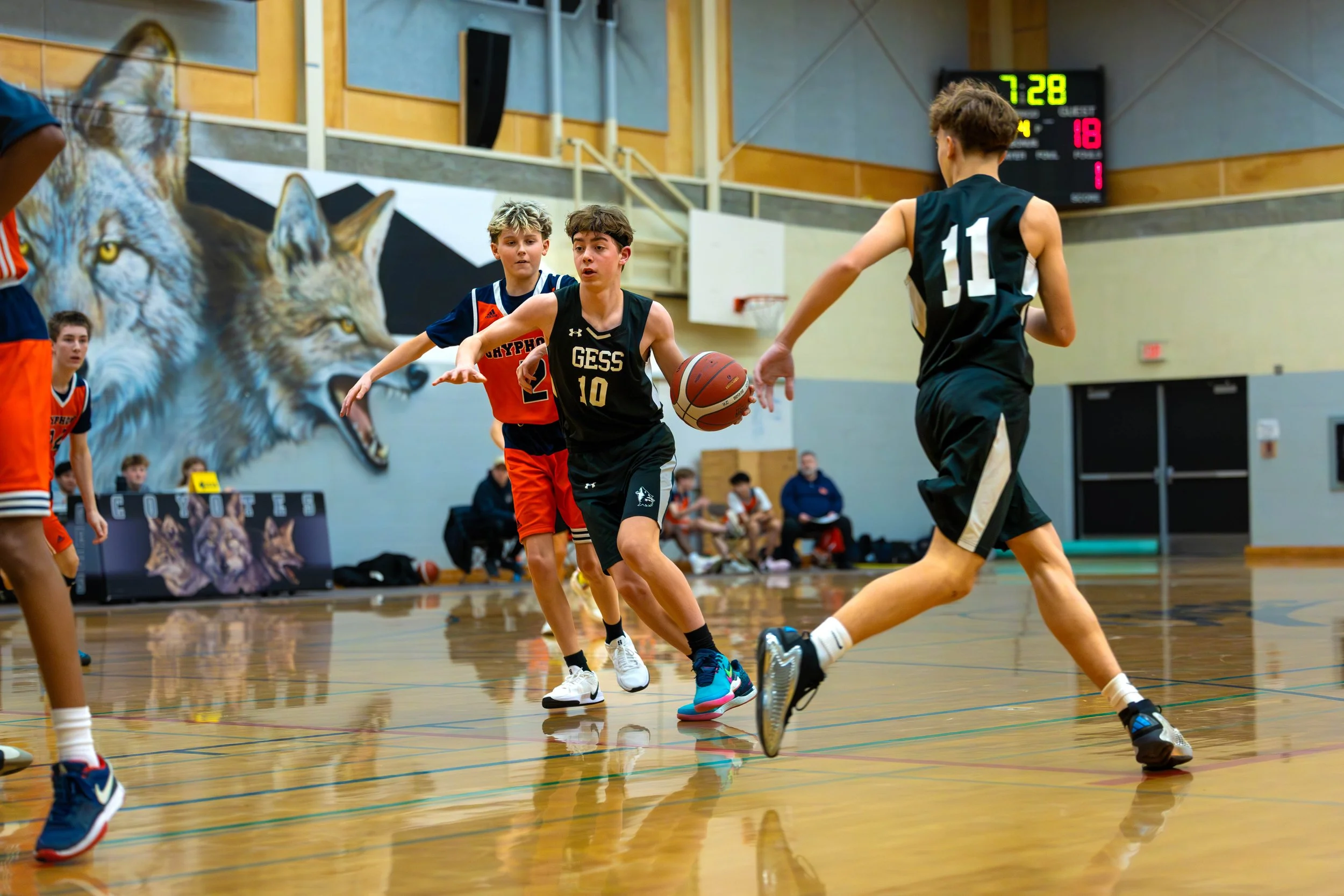 Young boys playing basketball in an indoor gymnasium with a wolf mural on the wall.