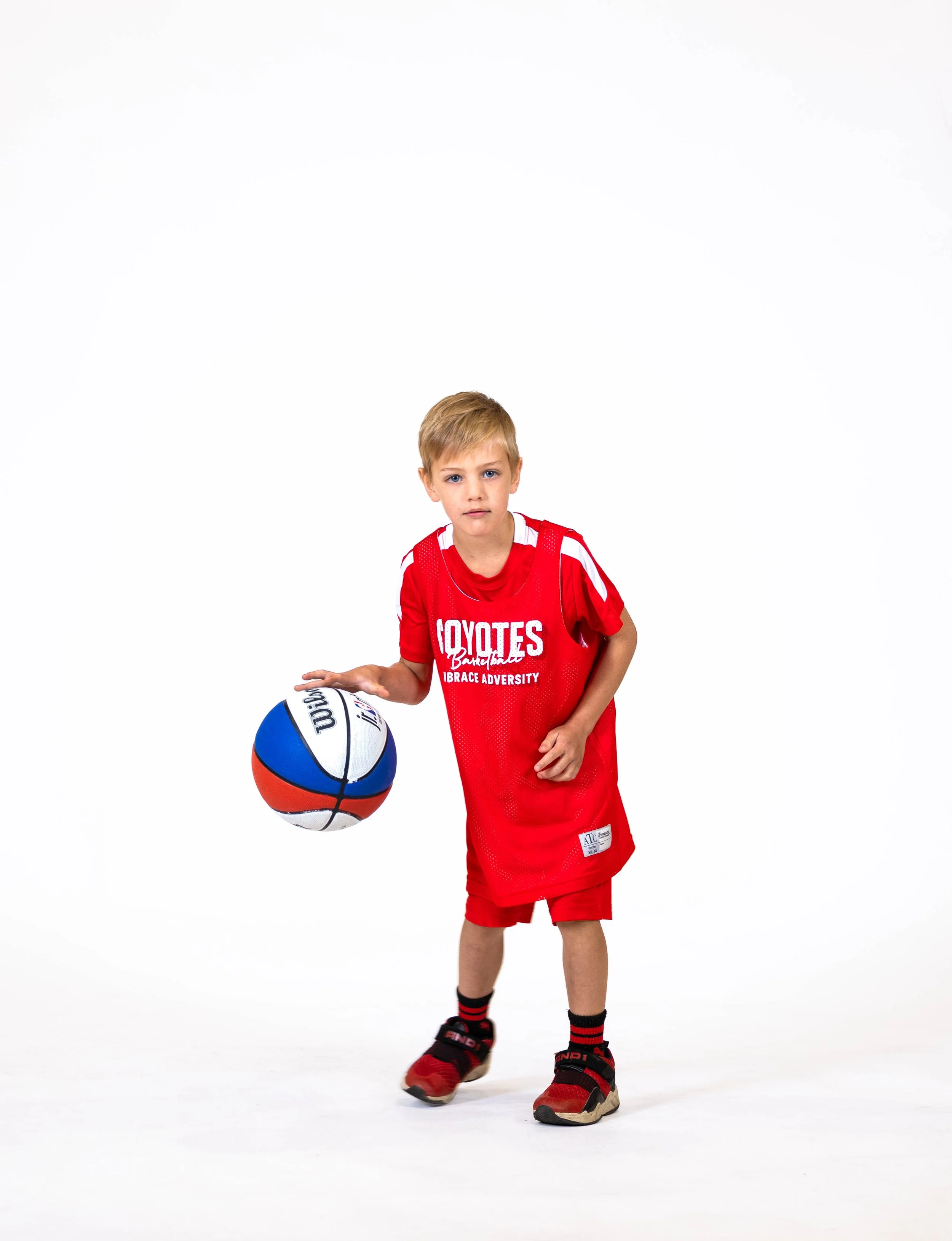 A young boy in a red sports uniform holding a basketball on a white background.