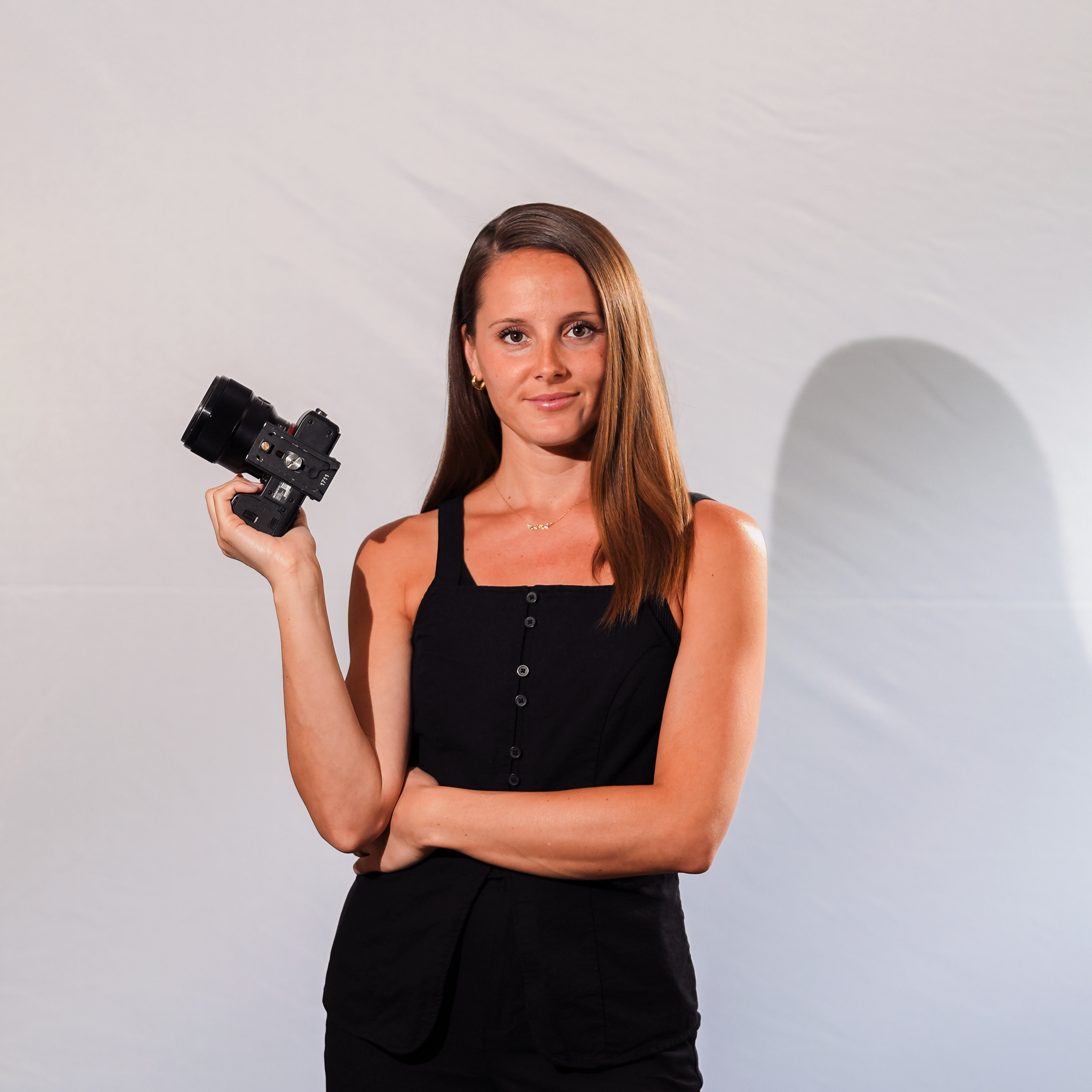 A woman holding a camera with a gimbal, standing next to a man wearing a headset, both smiling at the camera at an indoor event with purple lighting.