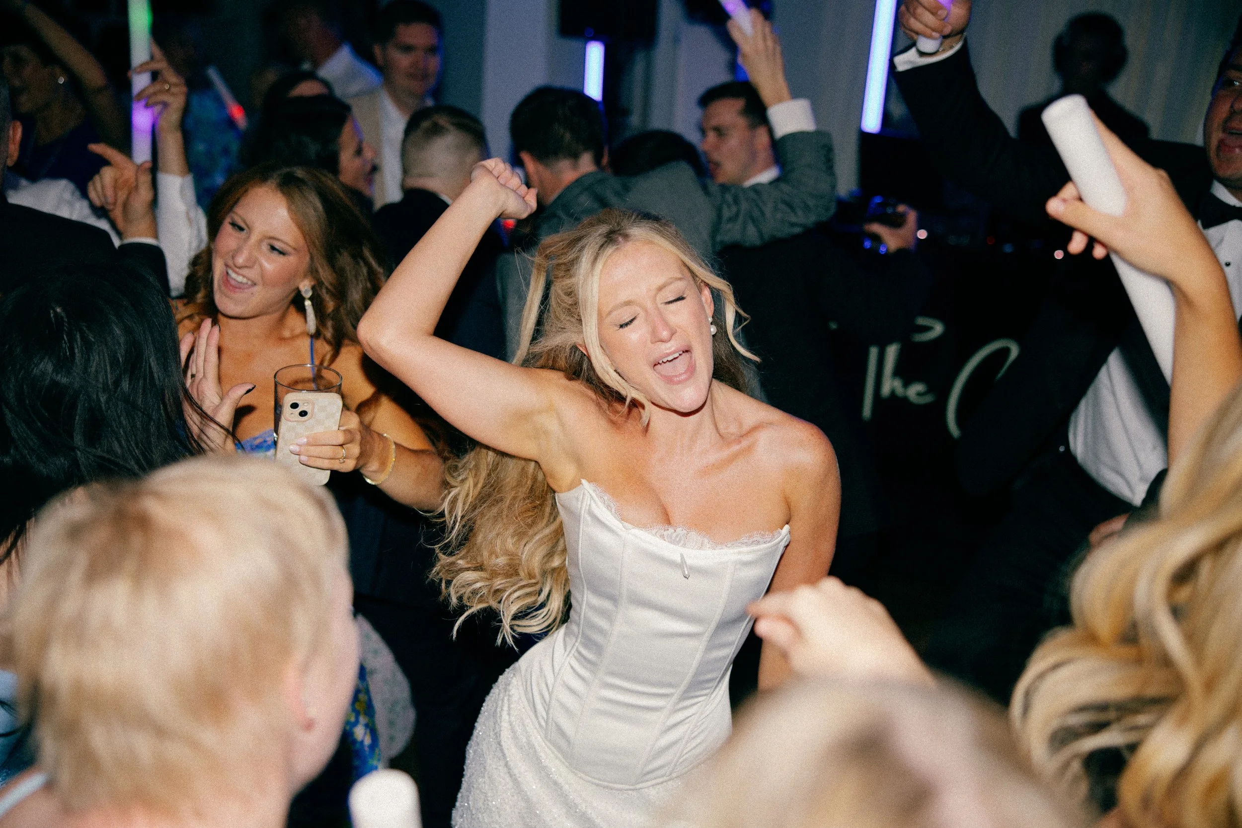 A woman dancing and singing with her eyes closed at a party, surrounded by other people dancing and enjoying the celebration.