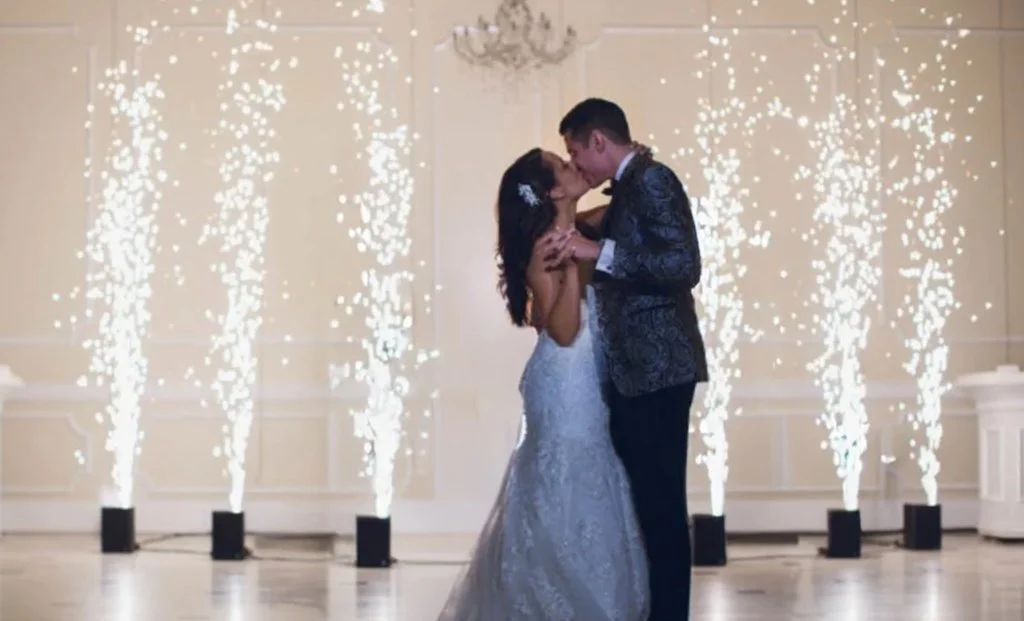 A bride and groom sharing a kiss on their wedding dance floor with white sparklers in the background.