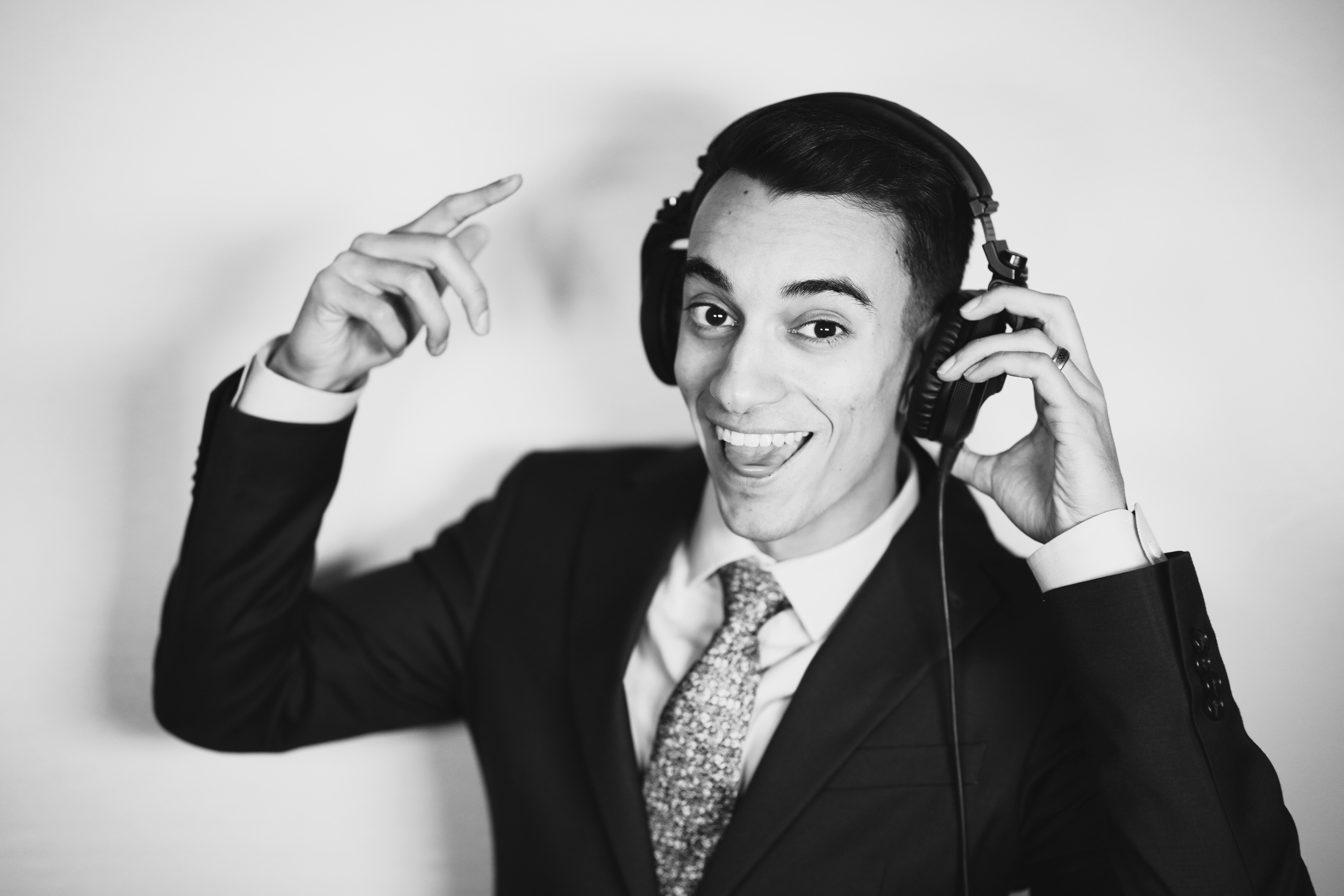 A young man in a suit wearing headphones, smiling and pointing at his head in a black and white photo.