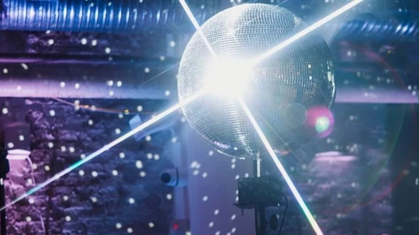 A disco ball reflecting light in a dark room decorated with purple and blue lighting.