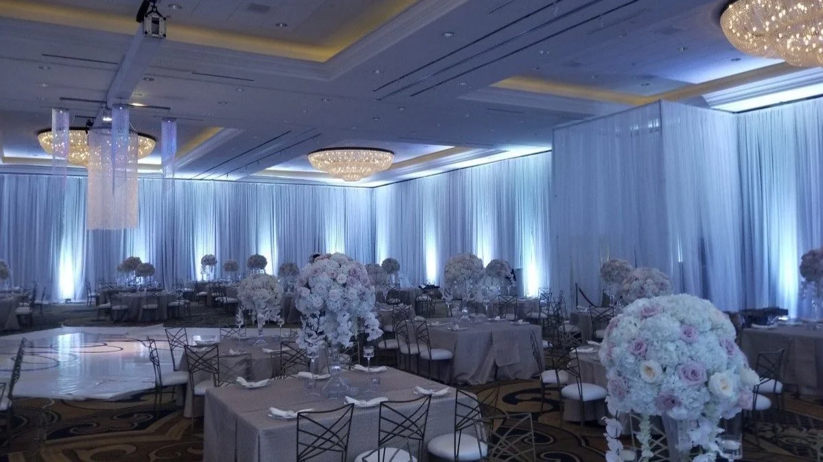 Elegant banquet hall decorated with blue drapes, large floral centerpieces, and round tables with white and gray tablecloths, set for a formal event.