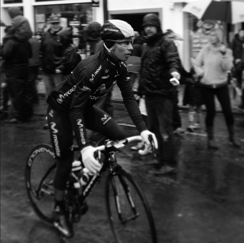 a black and white photo of a professional cyclist warming up before a race in the rain.