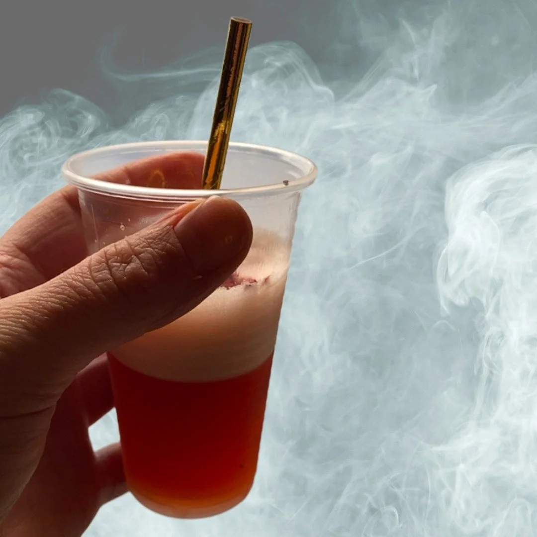 A hand holding a cocktail with a golden straw in it against a smokey background