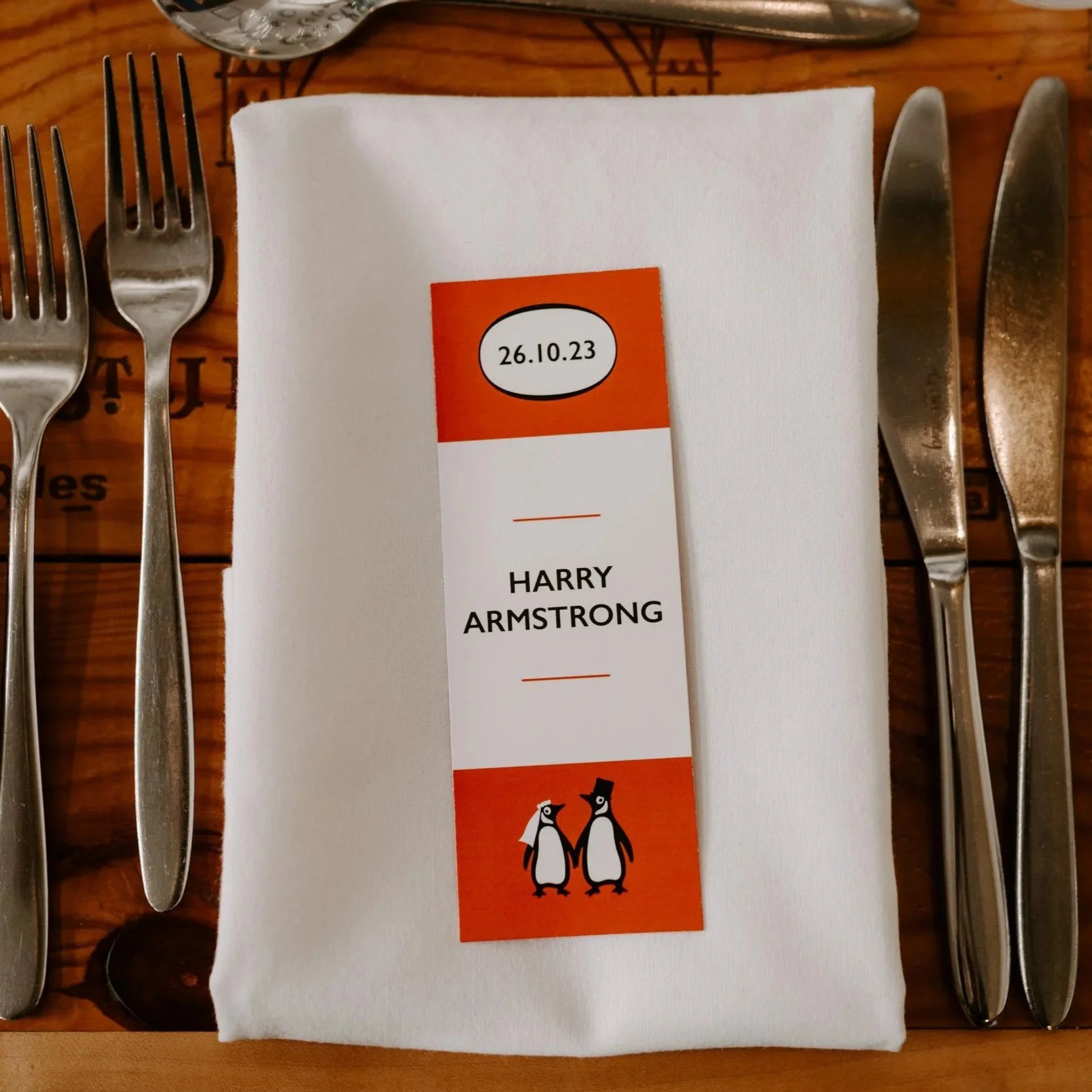 an orange and white book themed wedding bookmark place card sits on a white napkin as part of a place setting on a wooden table