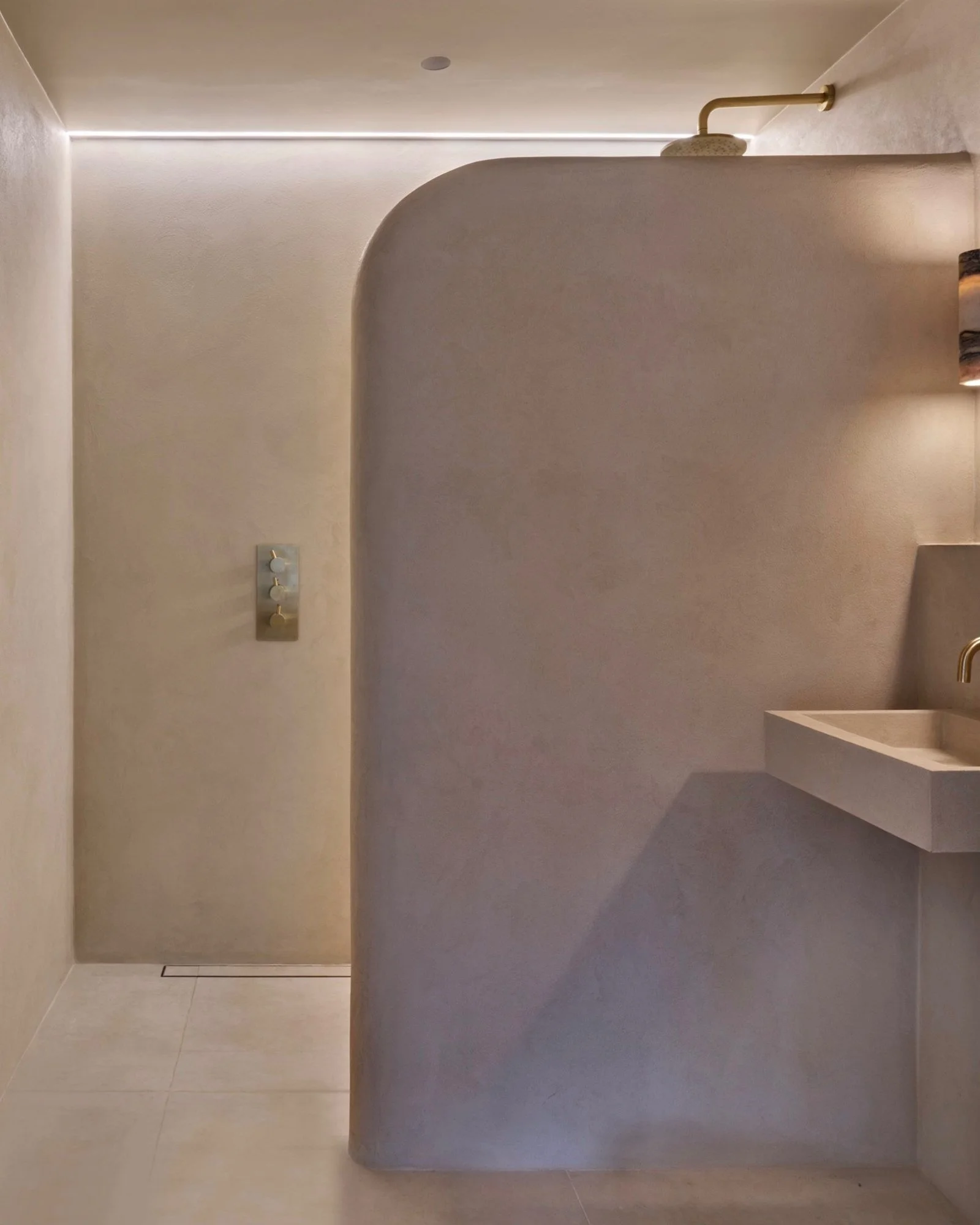 Walk-in shower with curved microcement partition wall, seamless microcement finish and brass shower fittings in Didsbury, Manchester.
