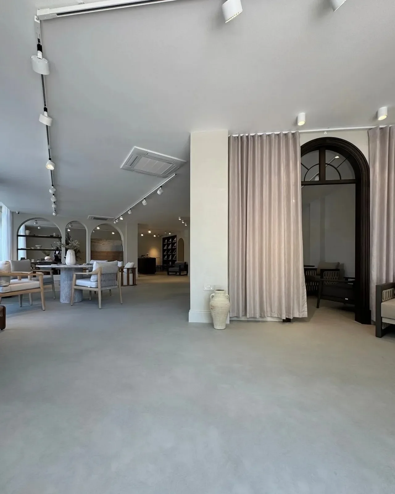 Modern interior space with seamless microcement flooring, neutral-toned furniture, and elegant archways creating a minimalist