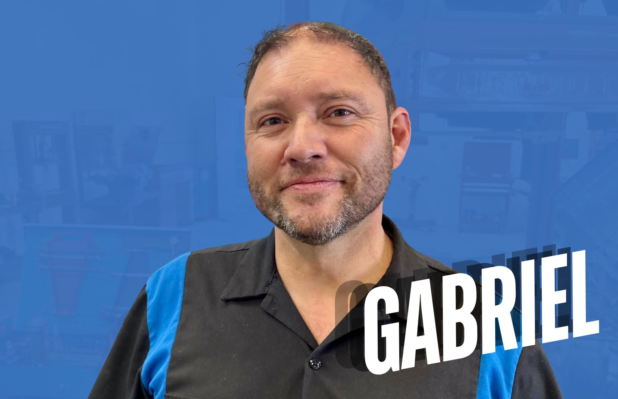 Man with short beard and dark hair smiling, wearing a black shirt with blue accents, standing in front of a blue background with the name 'Gabriel' in bold white letters.