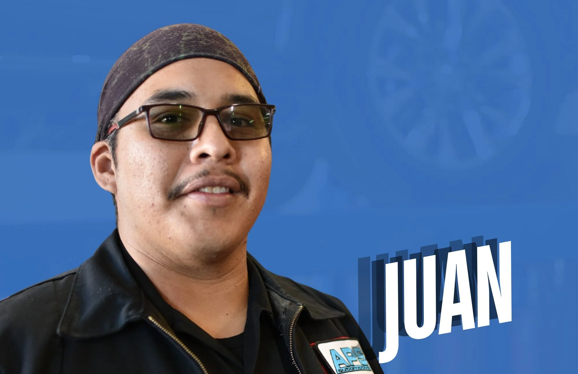 A man wearing glasses, a black leather jacket, and a dark headscarf, standing against a blue background with the name 'JUAN' in large white letters.