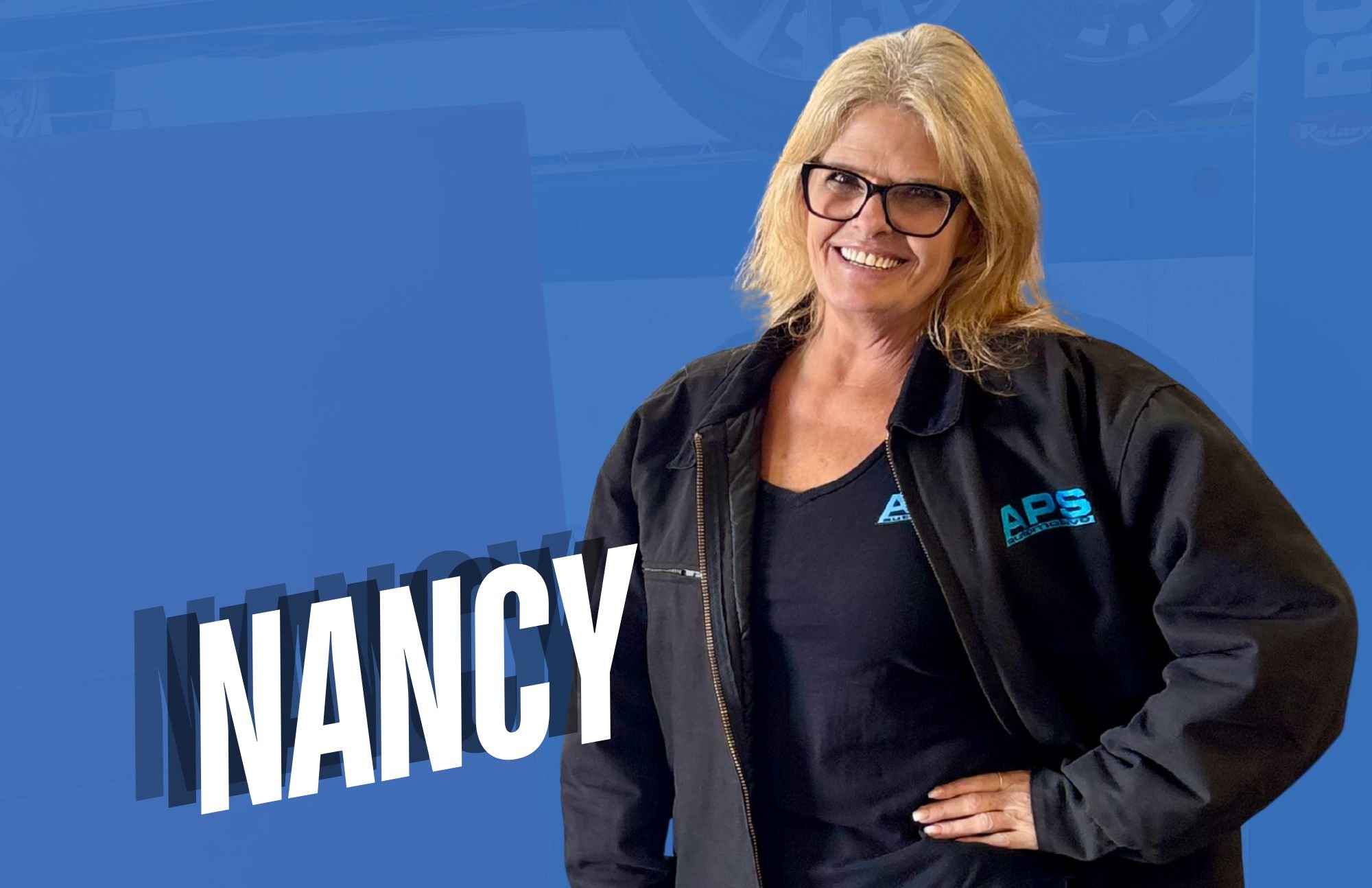 A woman with blonde hair wearing black glasses, a black shirt, and a black jacket with blue logo standing against a blue background. The text 'NANCY' is displayed in large white and black letters.