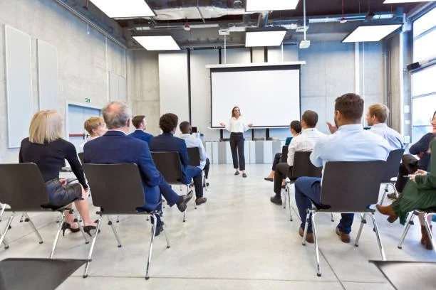 A woman giving a presentation to a seated audience in a modern conference room.