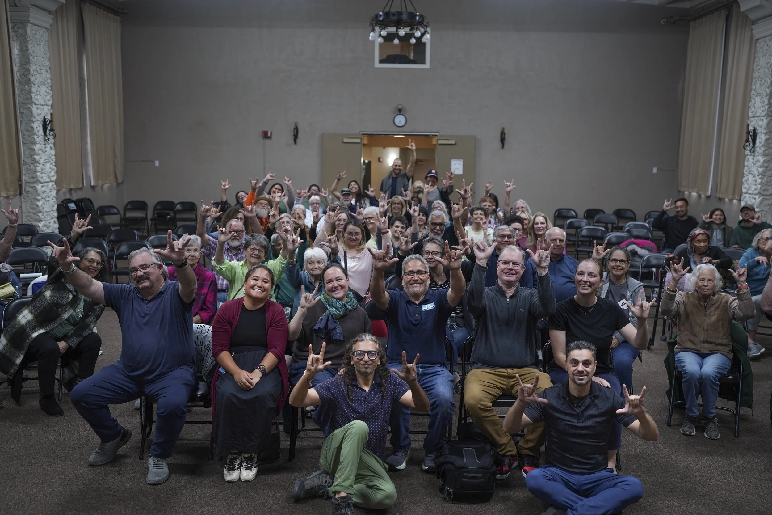 A large group of attendees pose together after a community screening of Being Michelle, smiling and making hand gestures that express solidarity, inclusion, and shared connection.