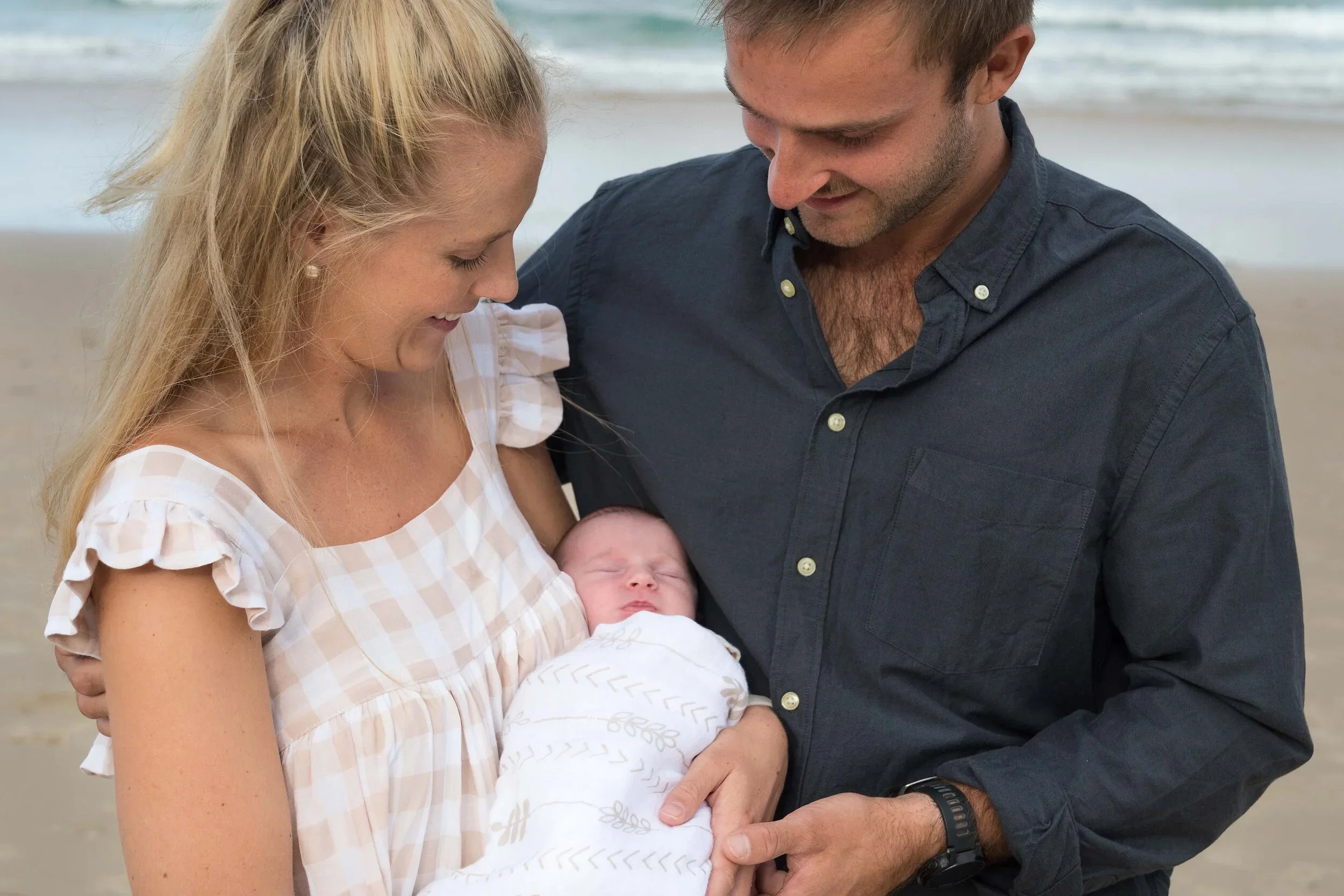 New parents holding their newborn baby together on the beach at Broadbeach.