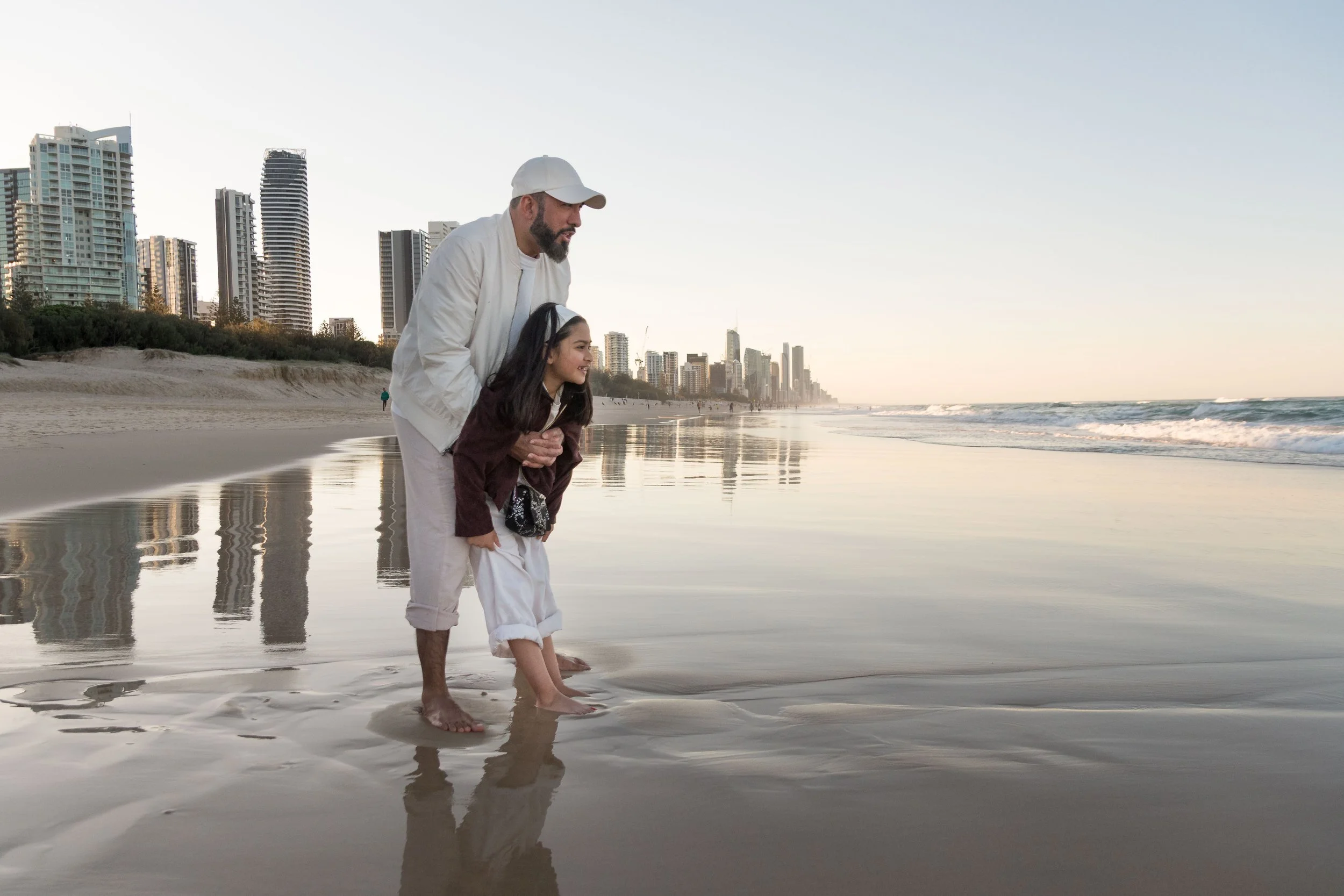A father and daughter enjoying a beach portrait session along the shore at Mermaid Beach with the Gold Coast skyline behind them, photographed by Scott Hardy