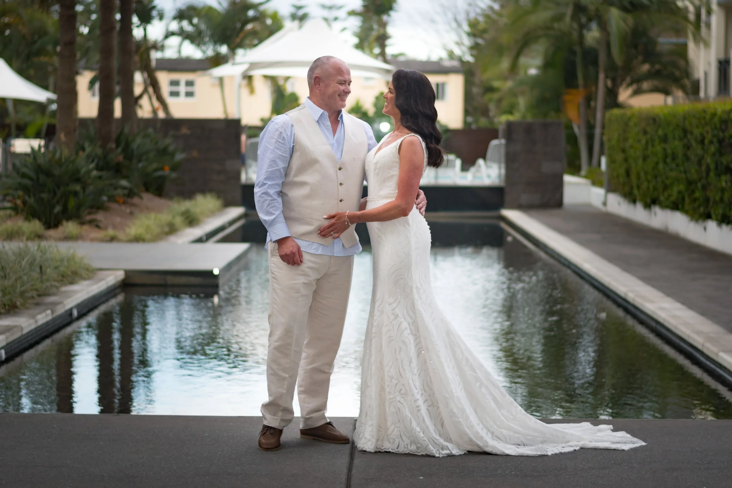 A bride and groom smiling at each other by the pool during their Ultra wedding in Broadbeach, captured by Gold Coast wedding photographer Scott Hardy