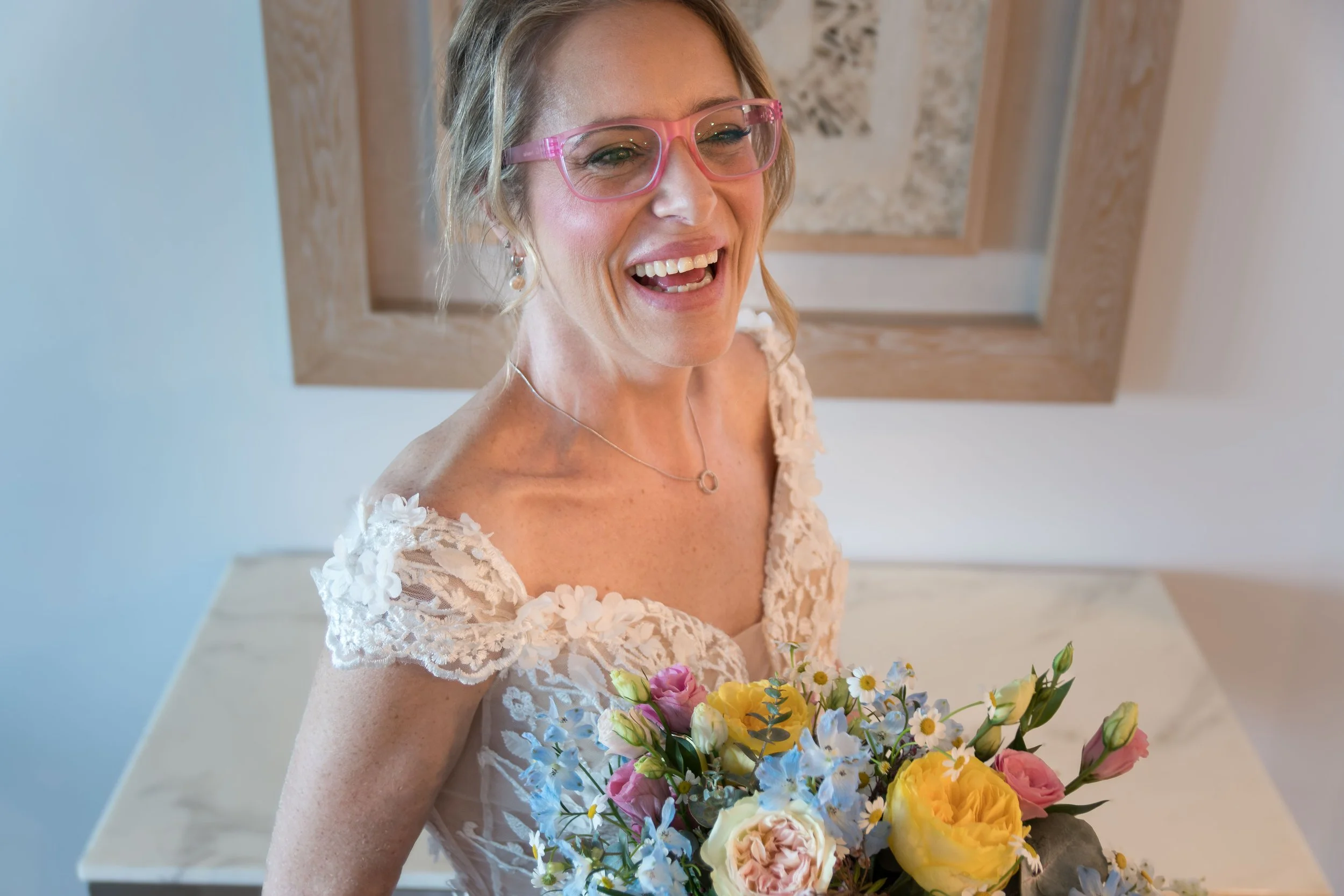 oyful bride wearing glasses and holding a vibrant floral bouquet preparing for her Gold Coast wedding.