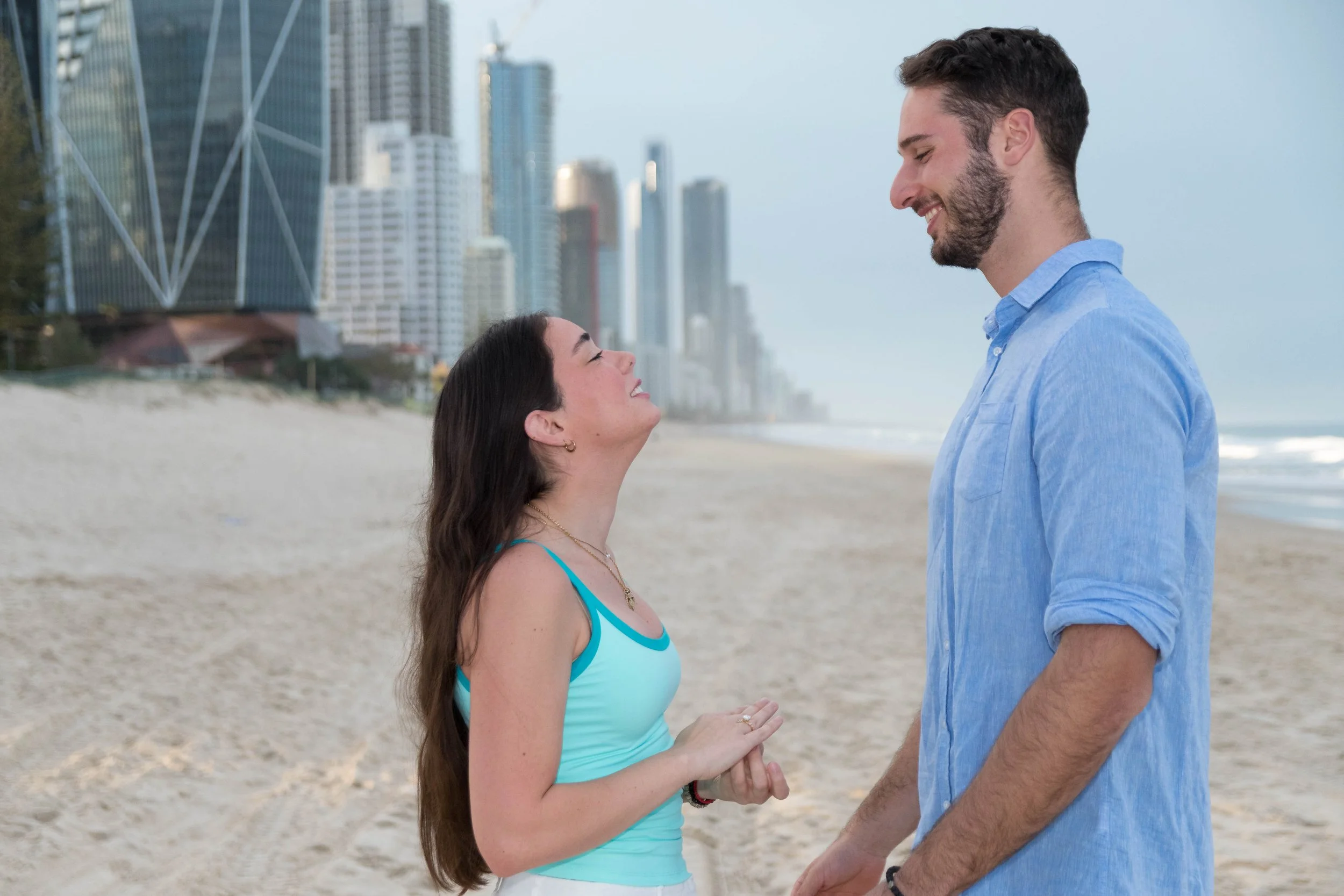 Engaged couple standing on the beach with the Surfers Paradise skyline during a Gold Coast engagement photography session.