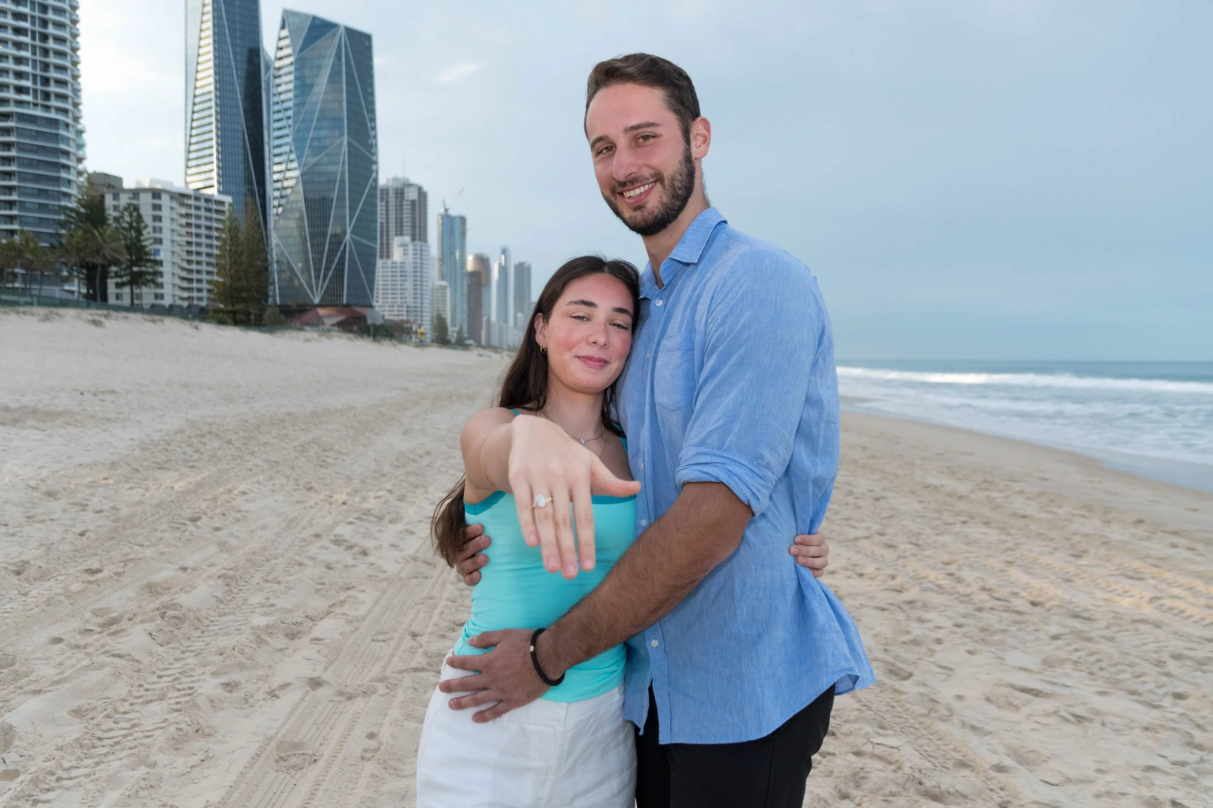 An engagement portrait session on the beach at Broadbeach with the Gold Coast skyline behind the couple, captured by Scott Hardy
